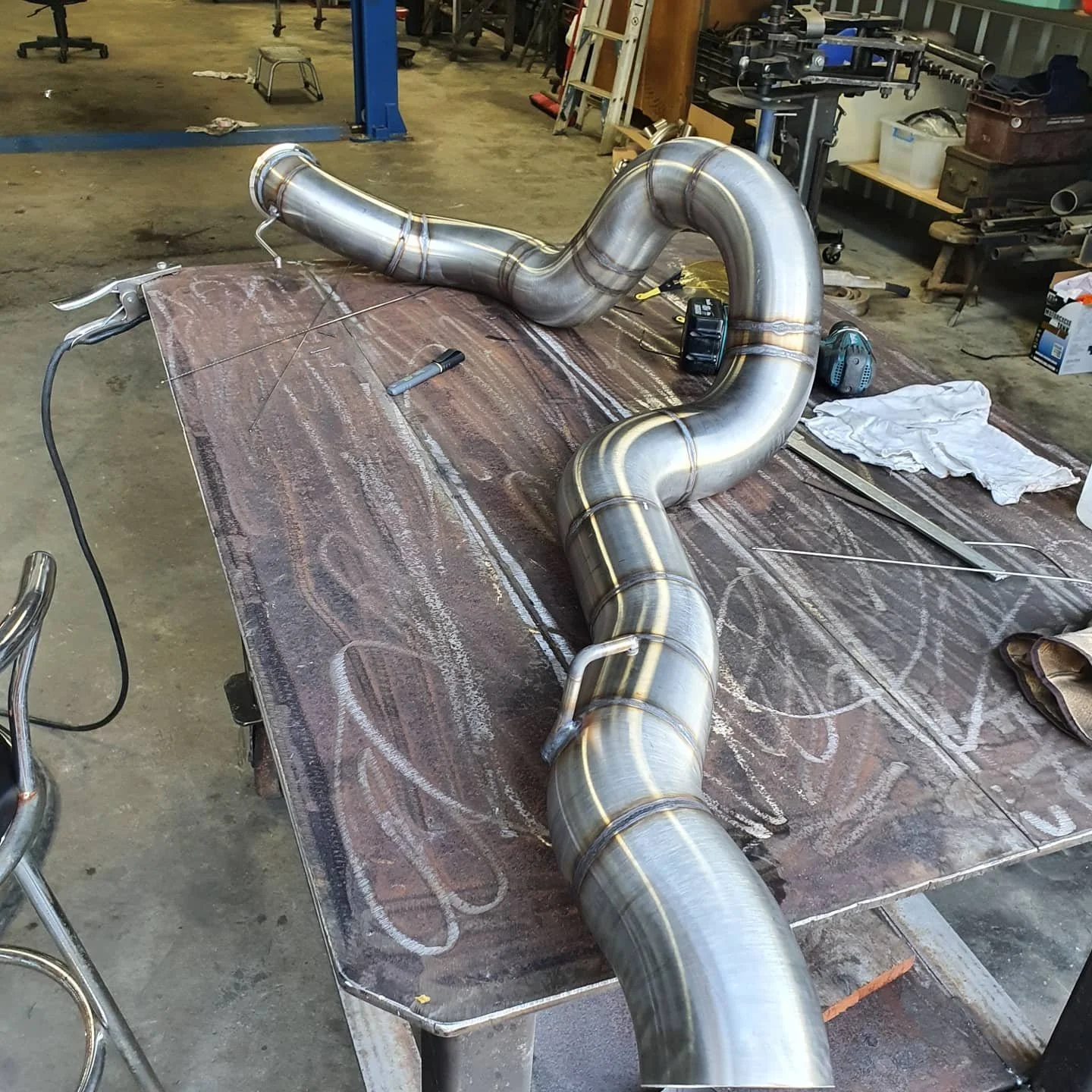 A large, bent metal exhaust pipe placed on a worktable in a workshop.