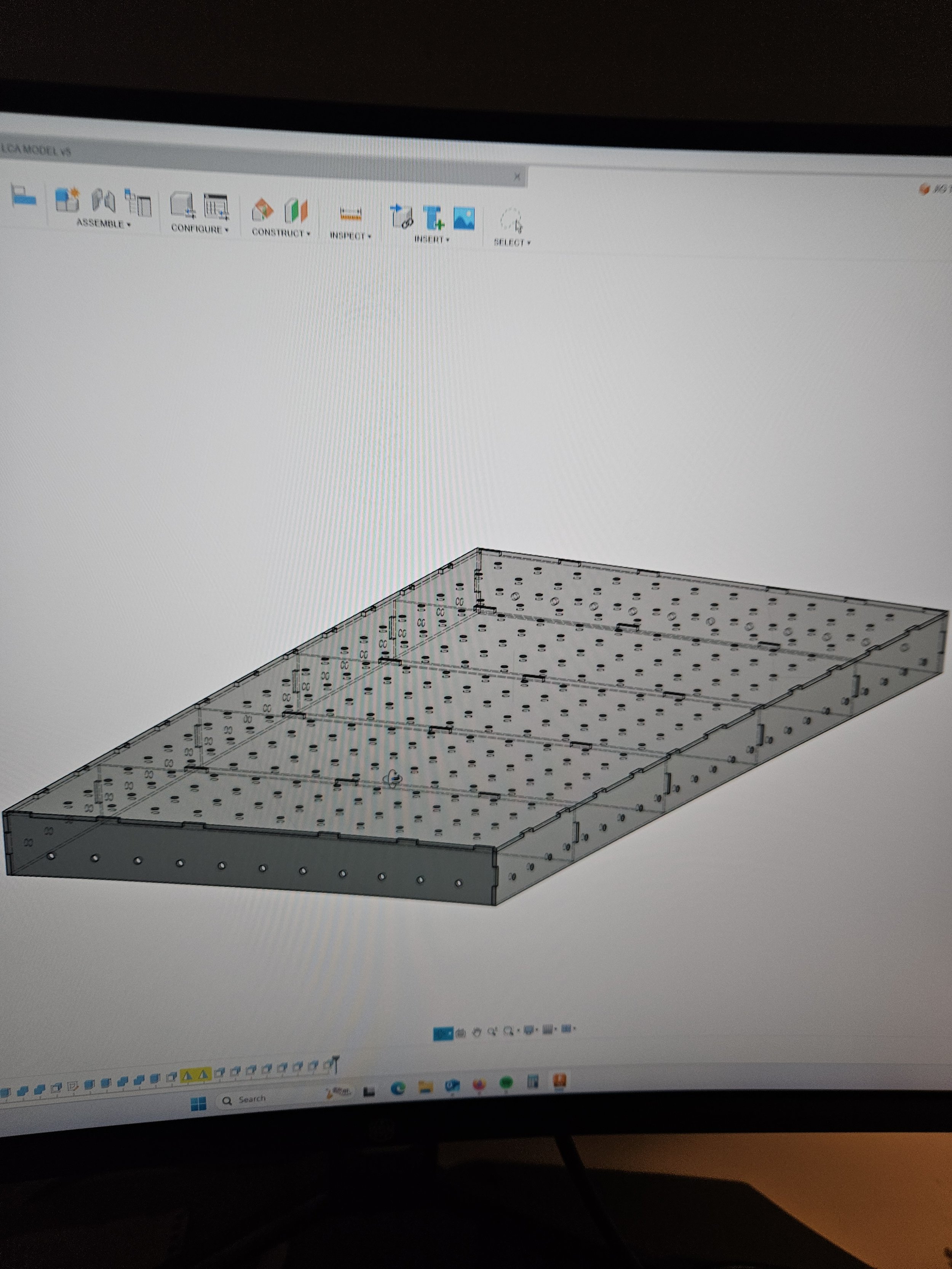 Computer screen displaying a 3D model of a rectangular metal enclosure with multiple holes and panels, created in CAD software.