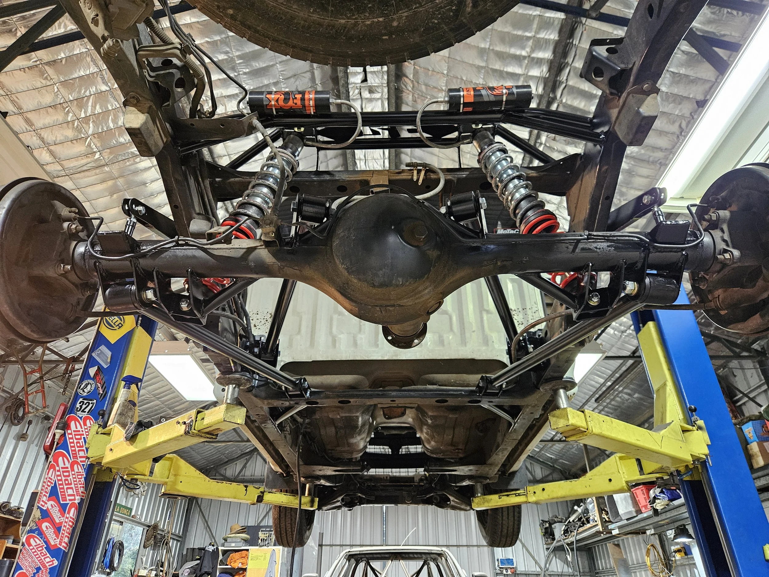 View of a vehicle's underbelly on a lift inside a garage, showing suspension components, axles, and part of the chassis.