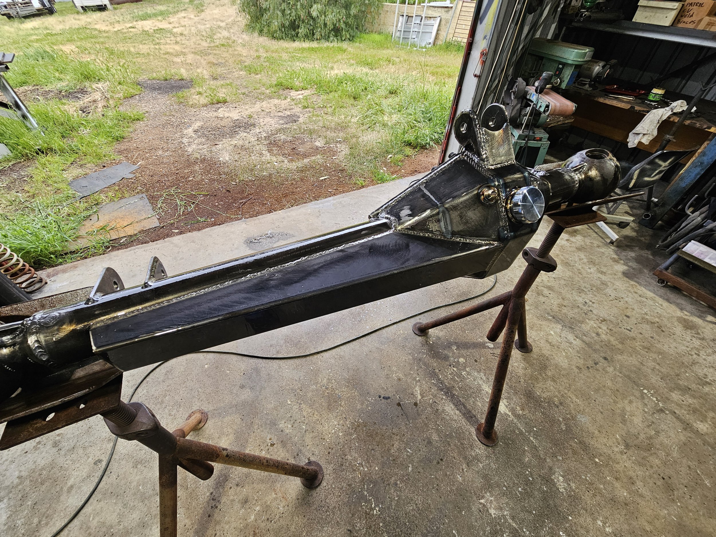 Metal structure or frame being constructed or repaired in a garage, supported by rusted stands with a partially assembled or modified device or machinery on top.