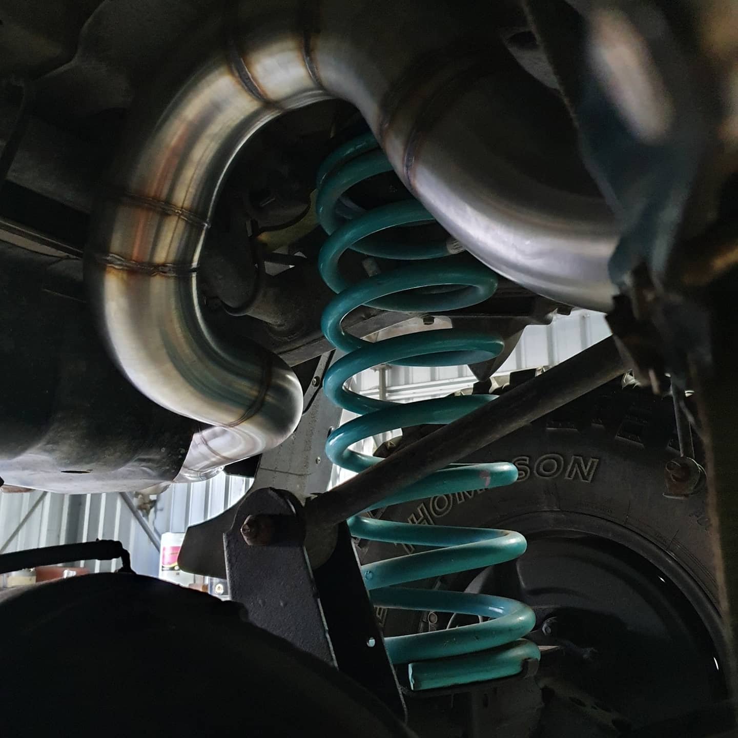 Close-up of a vehicle suspension system showing a turquoise coil spring and a metallic shock absorber in a garage.