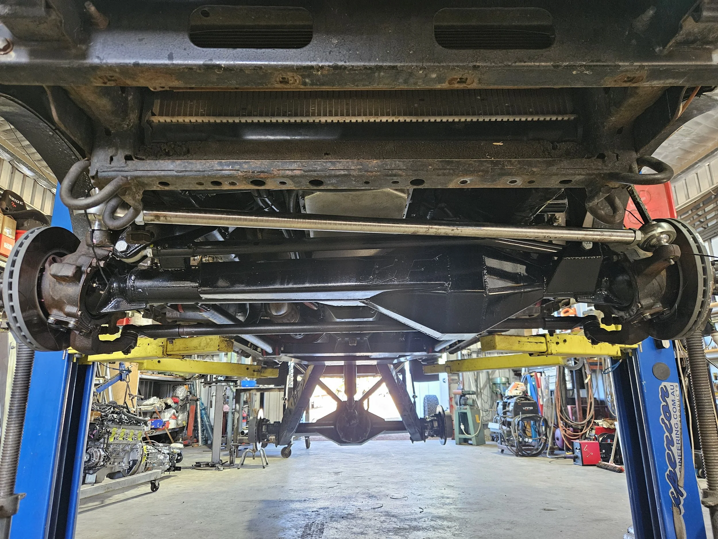 Underneath view of a vehicle on a hydraulic lift showing the suspension and differential components in an auto repair shop.