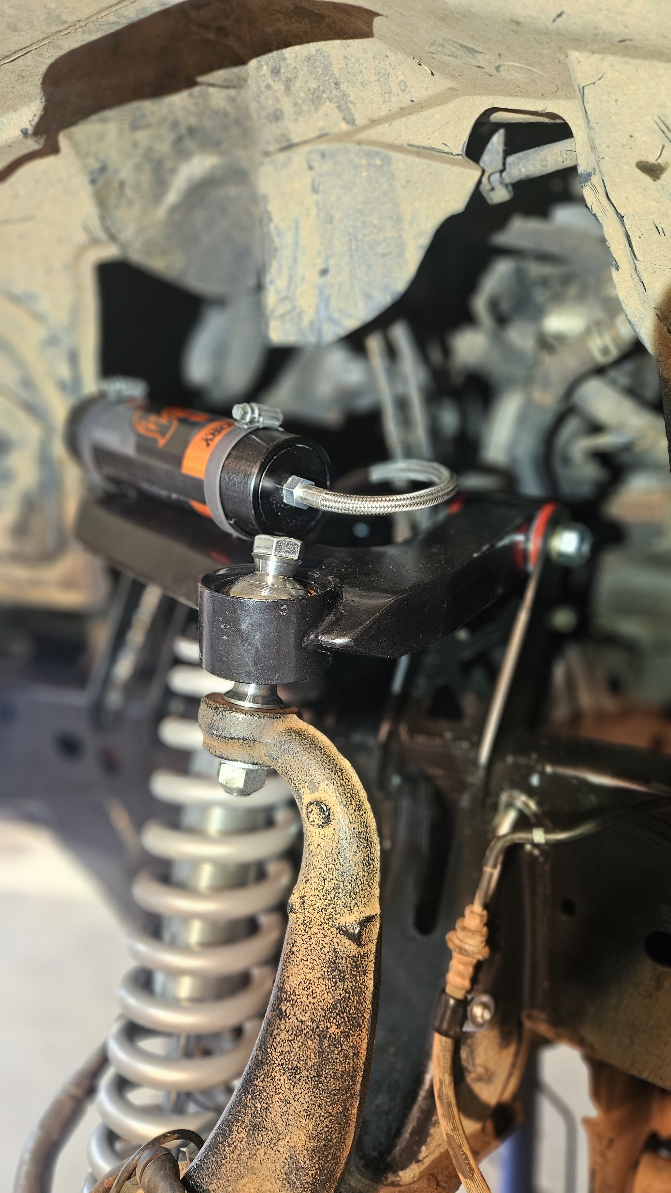 Close-up of suspension components on a vehicle, including a coil spring, shock absorber, and mounting hardware, with some parts showing rust and dirt.