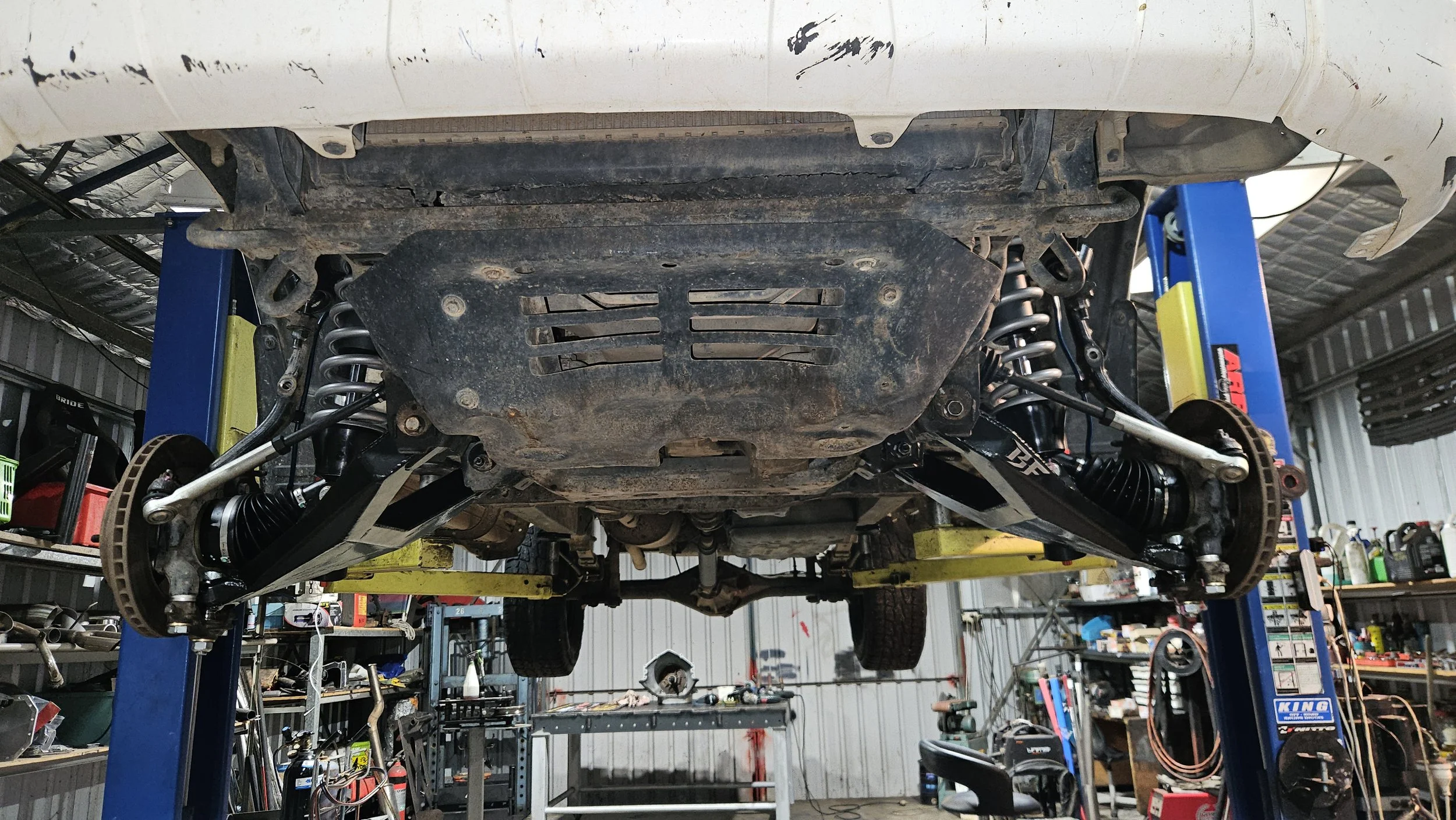 Underneath view of a car raised on a lift in a garage, showing suspension components and undercarriage.