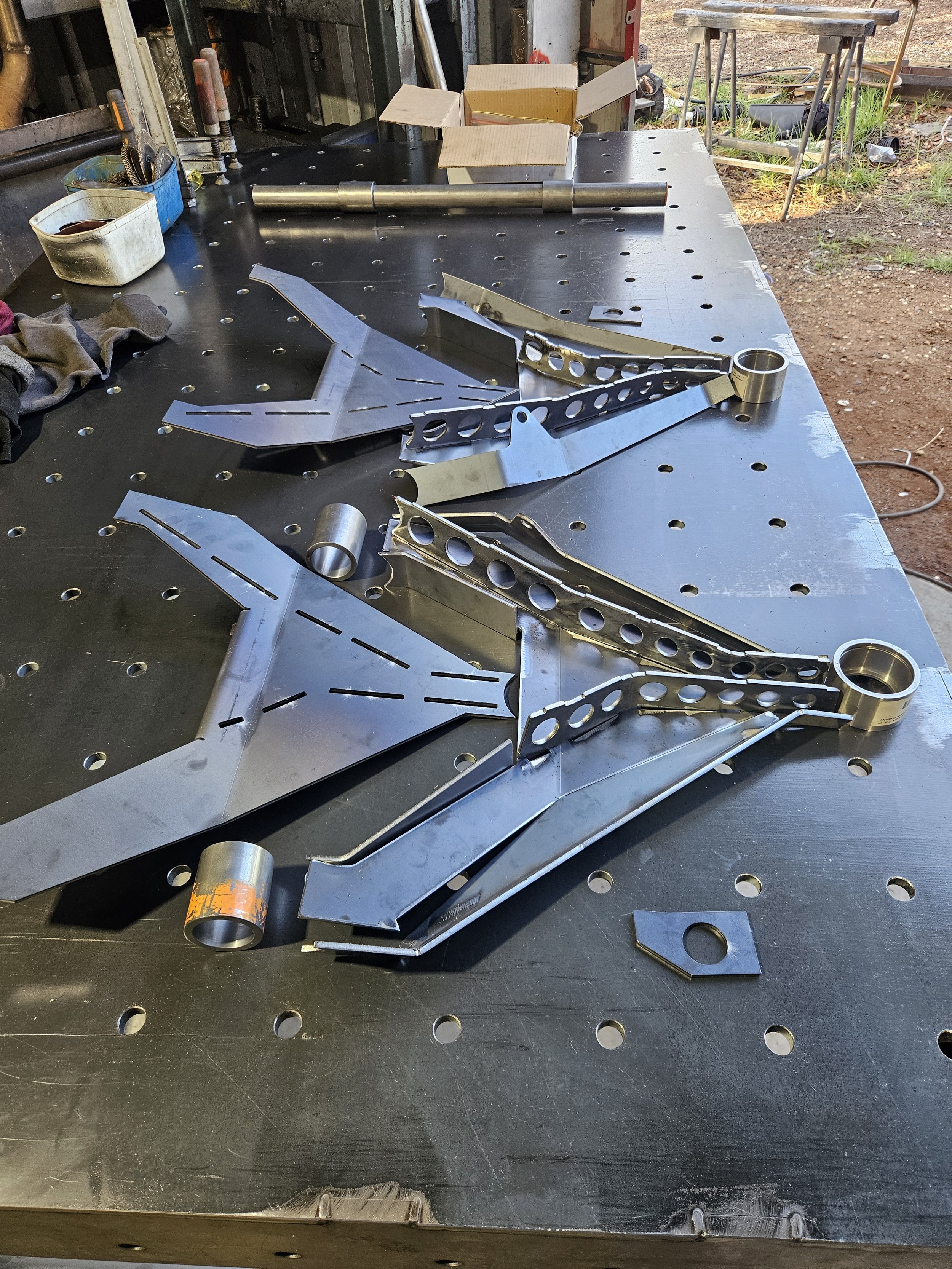 Metal parts and tools on a workbench in a workshop, with an outdoor area visible in the background.