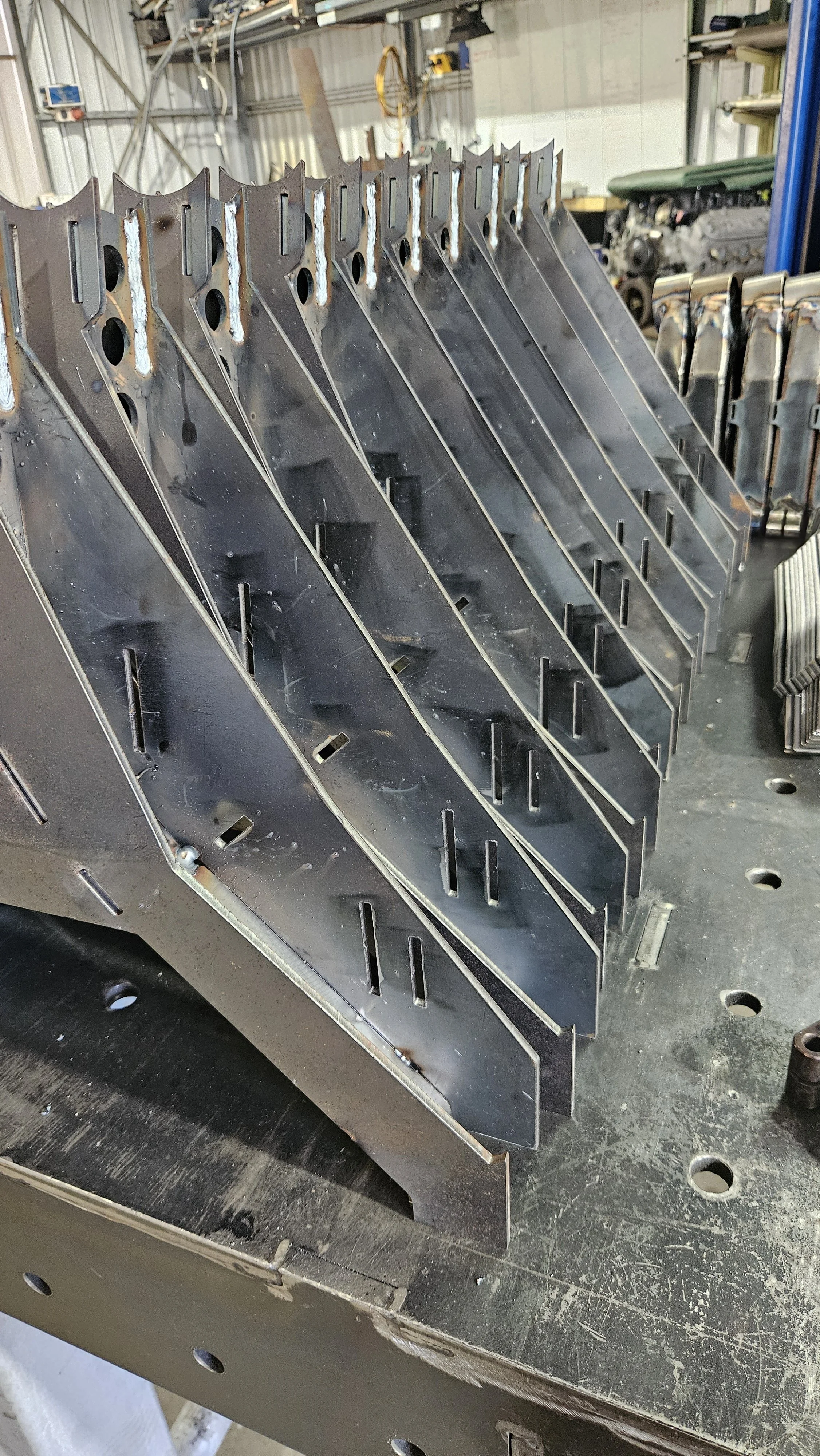 Metal parts with slots and holes, likely components for machinery or vehicle construction, placed on a workbench in a workshop.