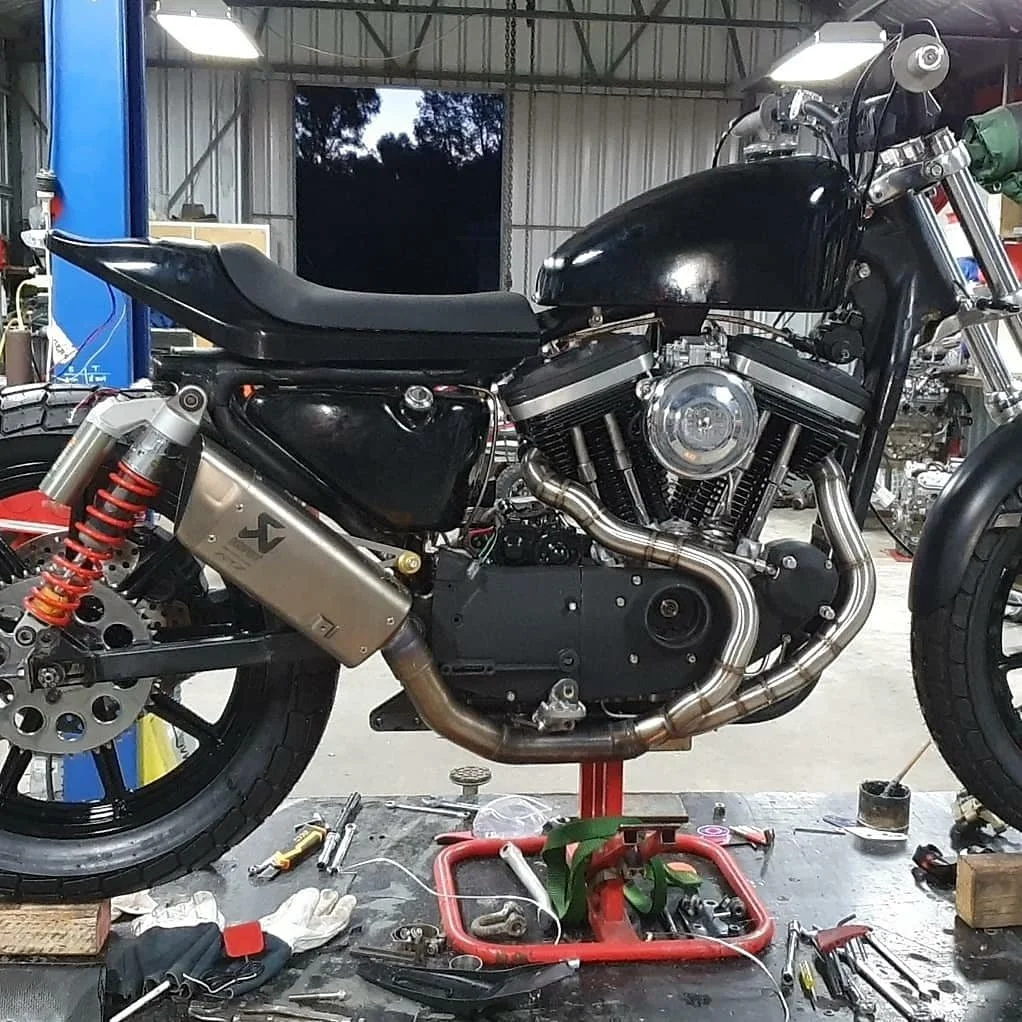 Motorcycle in a workshop, partially assembled with tools and equipment on a workbench.