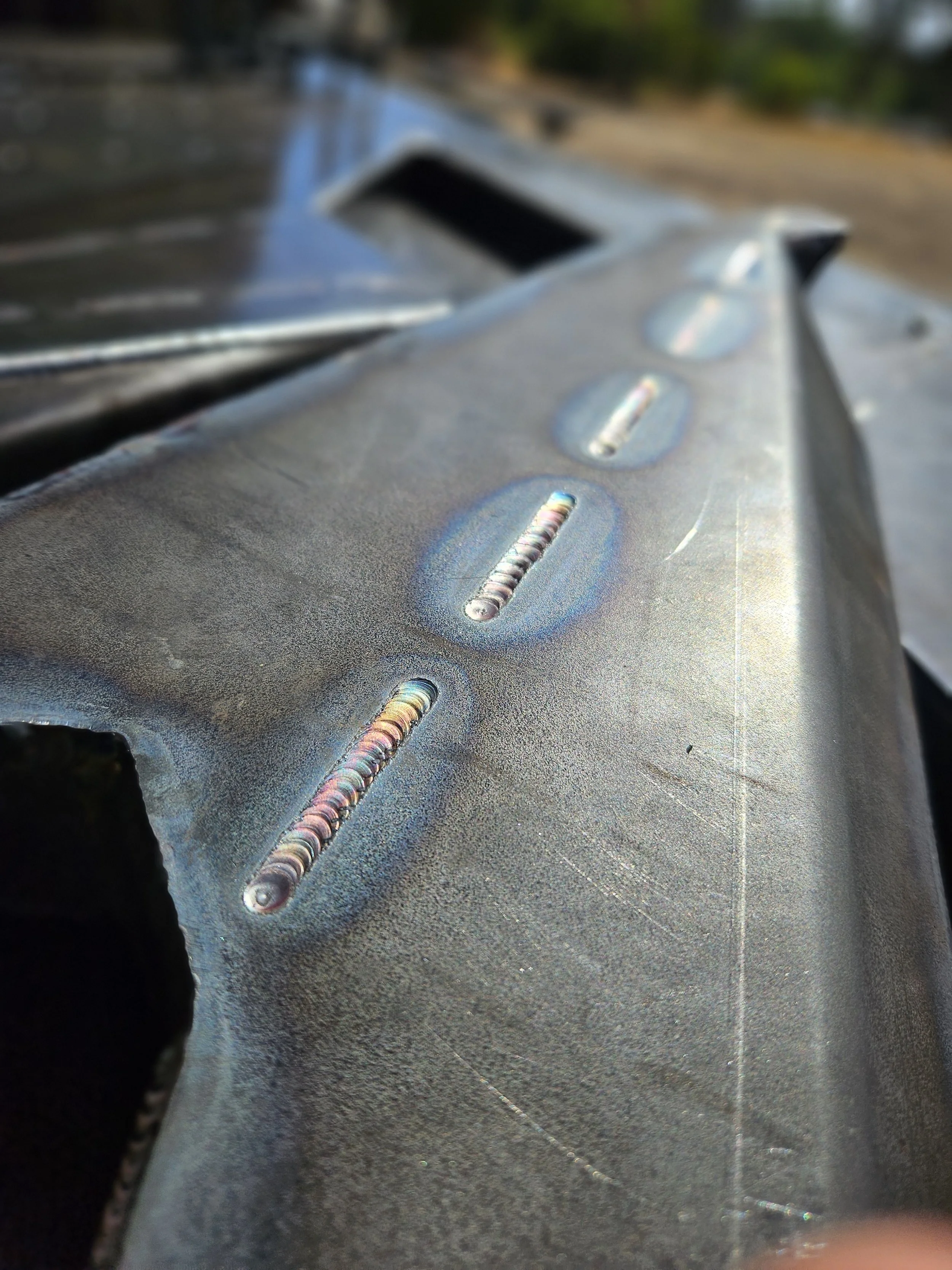 Close-up of a metallic surface with laser welds, likely part of a vehicle or machinery, with blurred background.