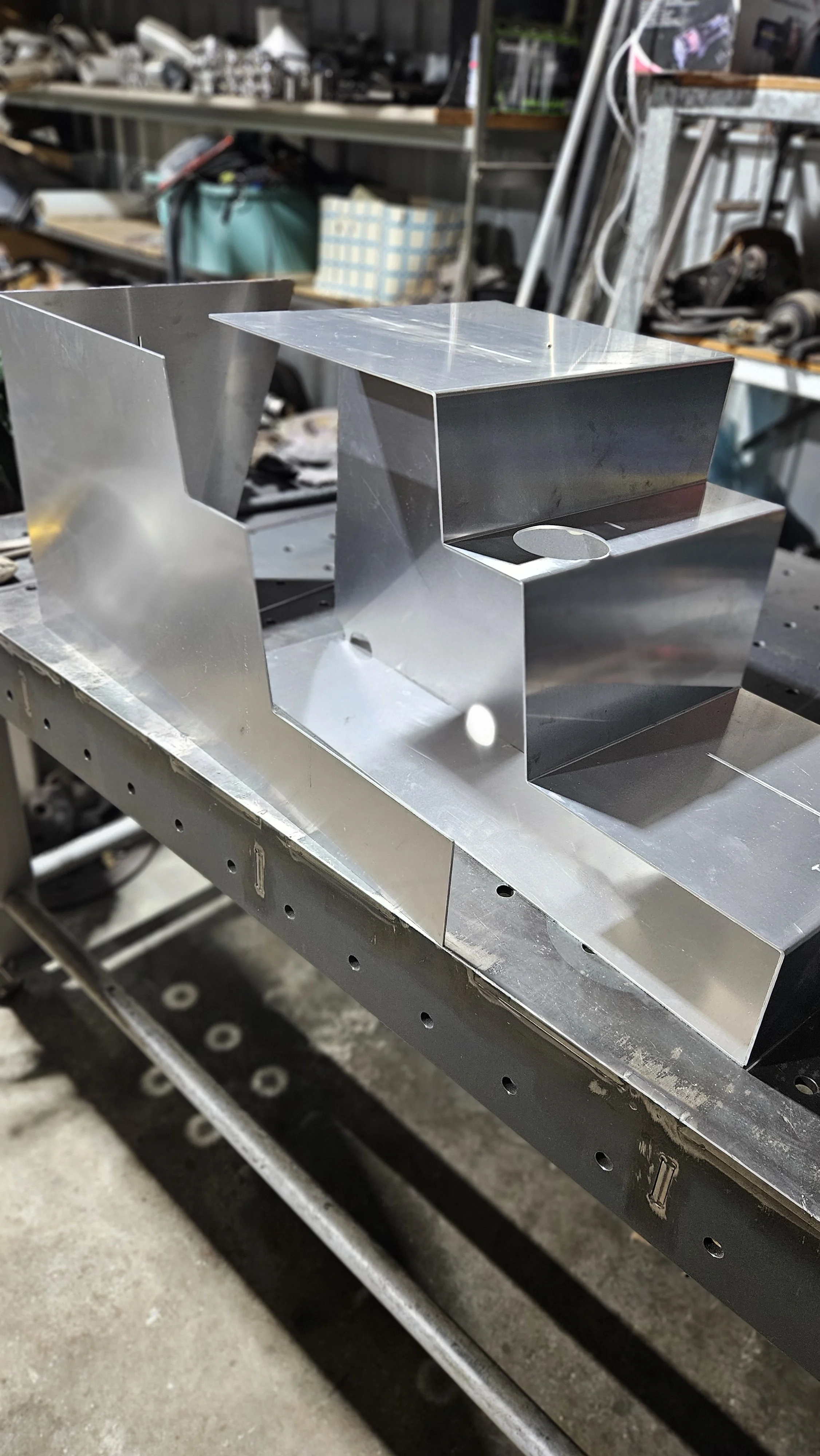 Close-up of a metal workshop with a shiny, unfinished metallic structure on worktable, surrounded by tools and workshop materials in background.