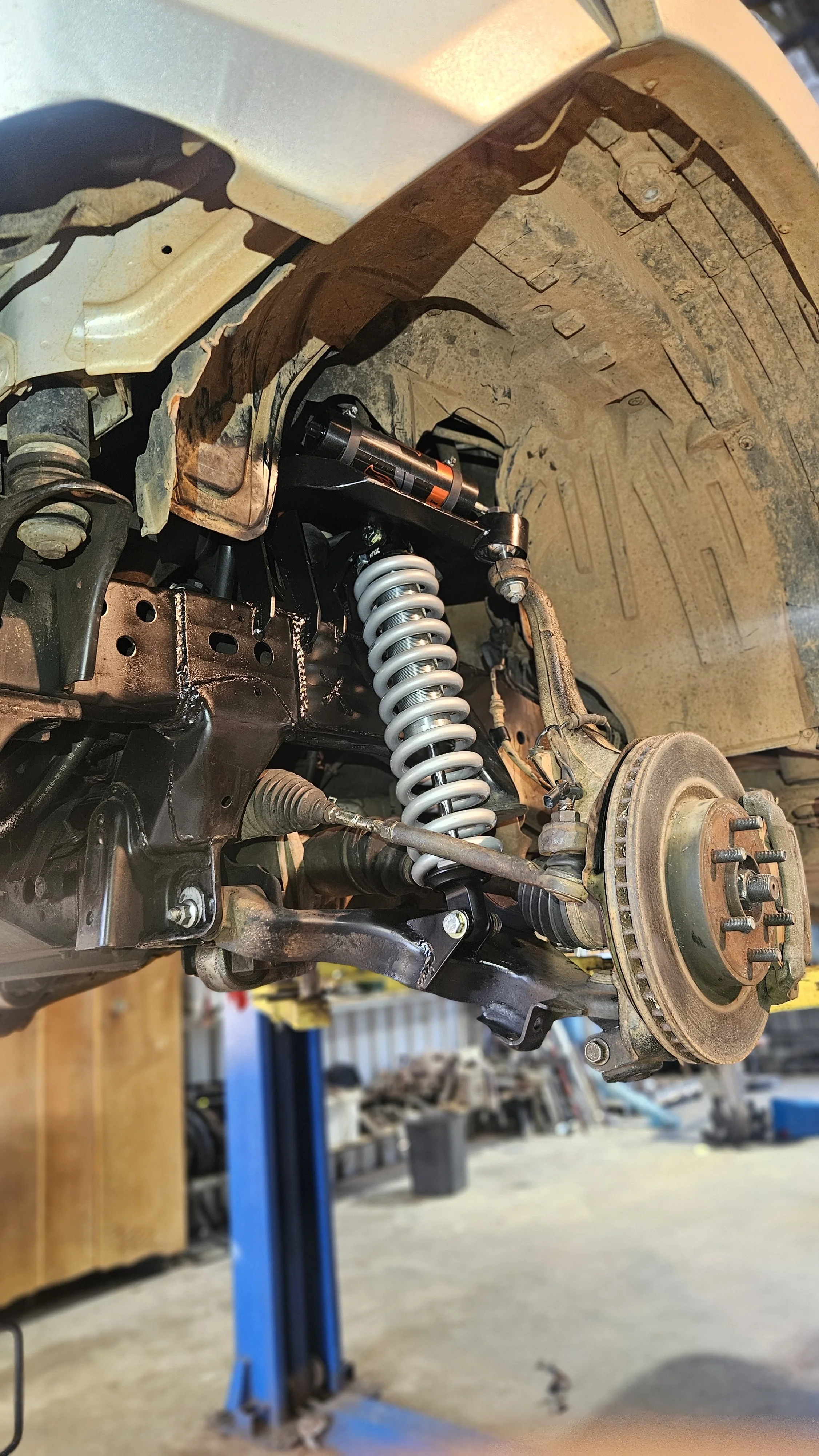 Suspension and brake components of a vehicle's wheel assembly, with the wheel removed, in a garage.