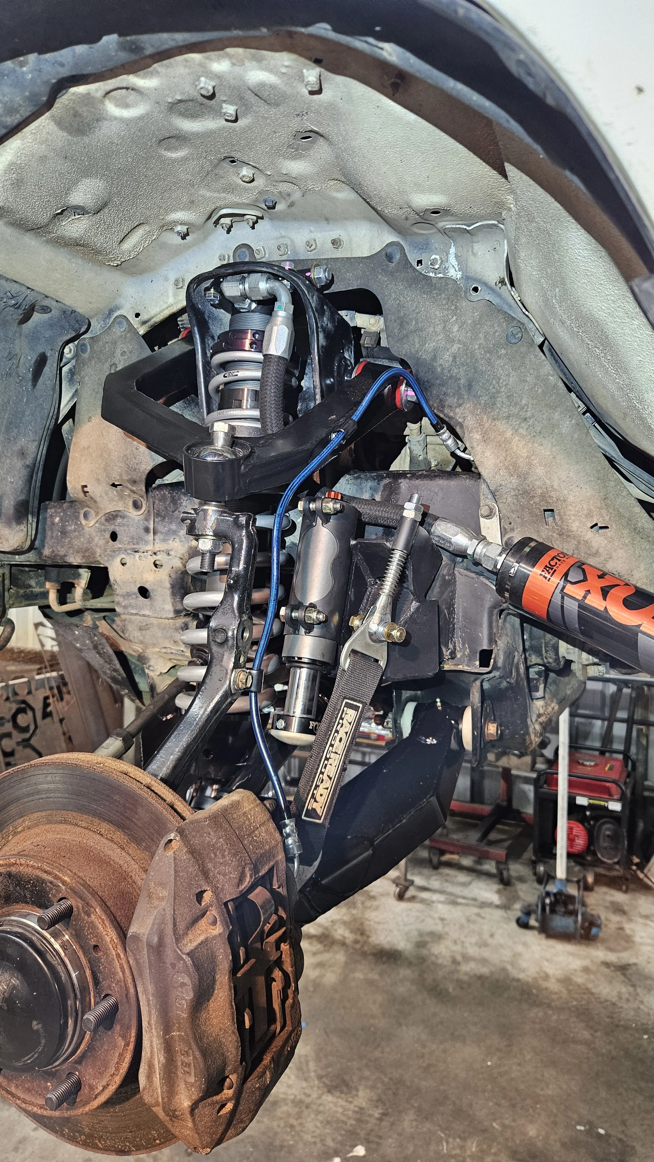Close-up view of a car suspension system with coil spring, shock absorber, and brake rotor without brake caliper, in a garage workshop.