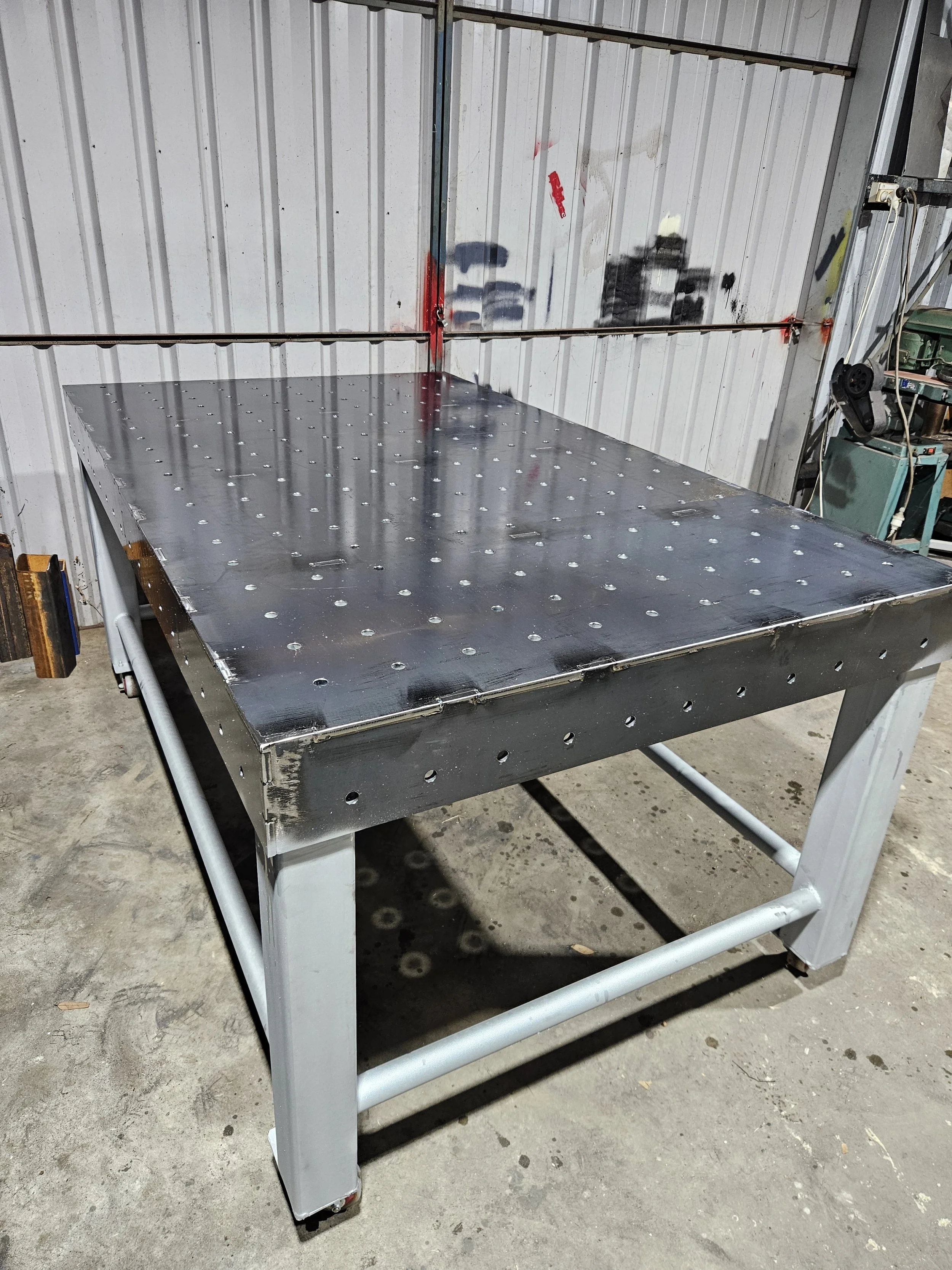 Metal work table with a pegboard surface and sturdy white legs in a workshop setting.