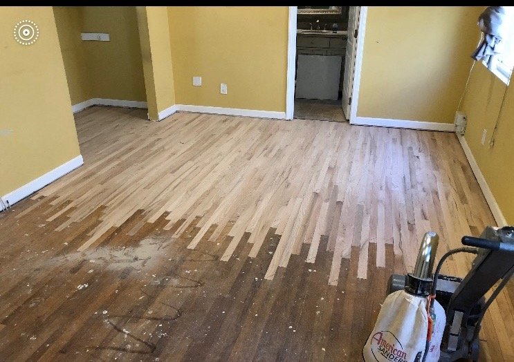 Room with yellow walls and wooden floor being refinished, with the new floor partially installed, vacuum cleaner in the corner.