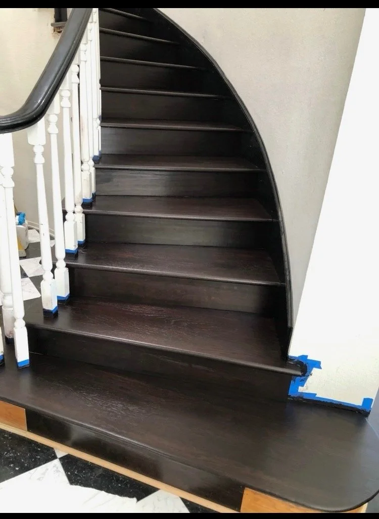 Dark brown wooden staircase with a white balustrade on the side, showing some tape on the bottom right corner.