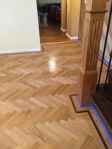 Beautiful hardwood floor in a house with a chevron pattern, next to a staircase with wood and metal railing.