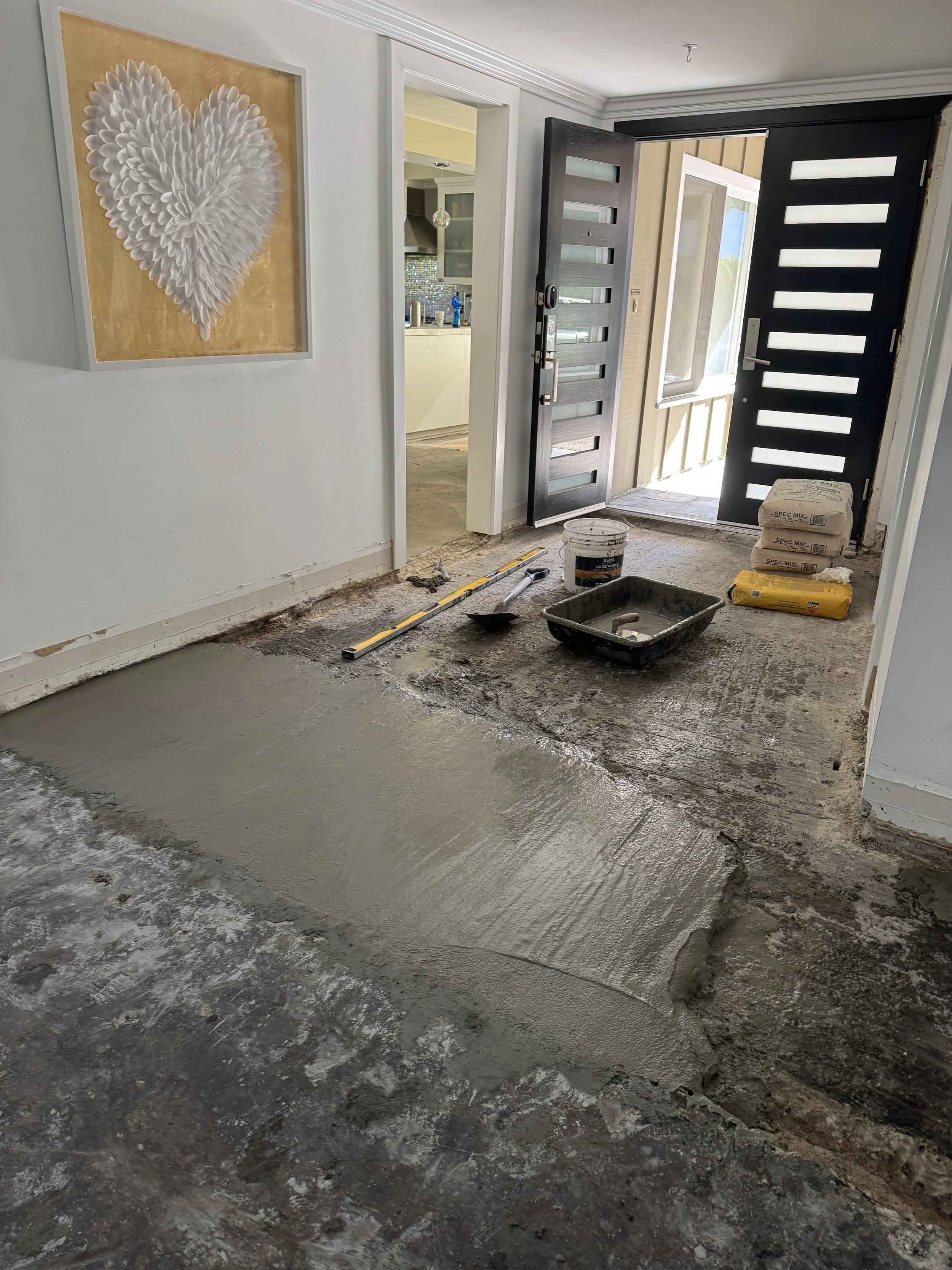 Entryway with a partially poured concrete floor, construction tools, and materials for a renovation.
