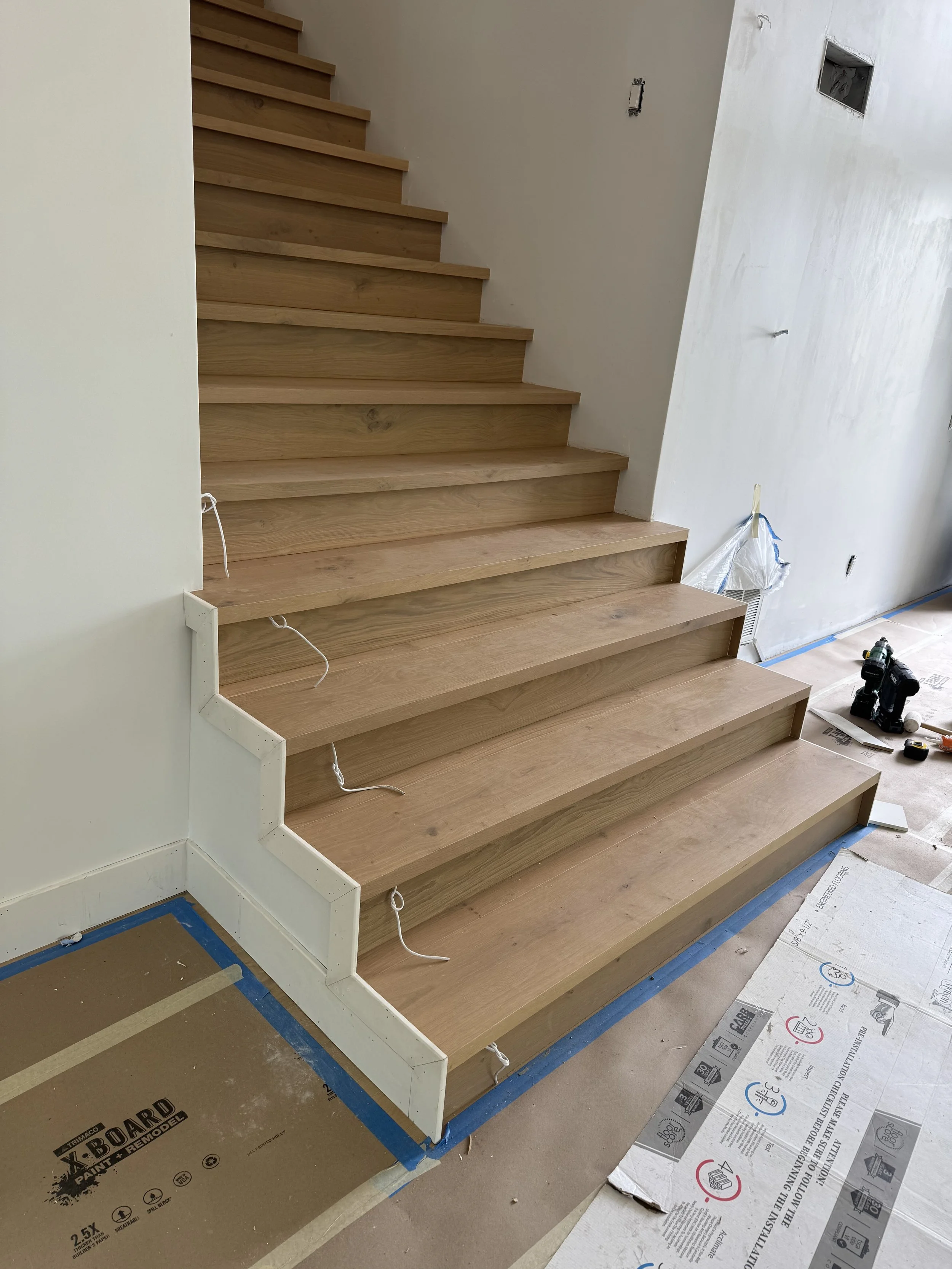 Wooden staircase under construction with white risers, partially finished steps, and construction tools and materials on the floor.