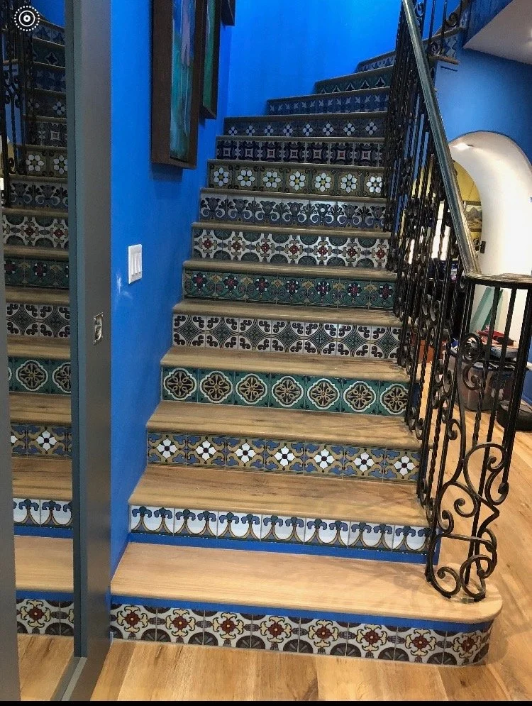 Interior staircase with decorative tiles on the risers, metal railing, wooden steps, and a blue wall.