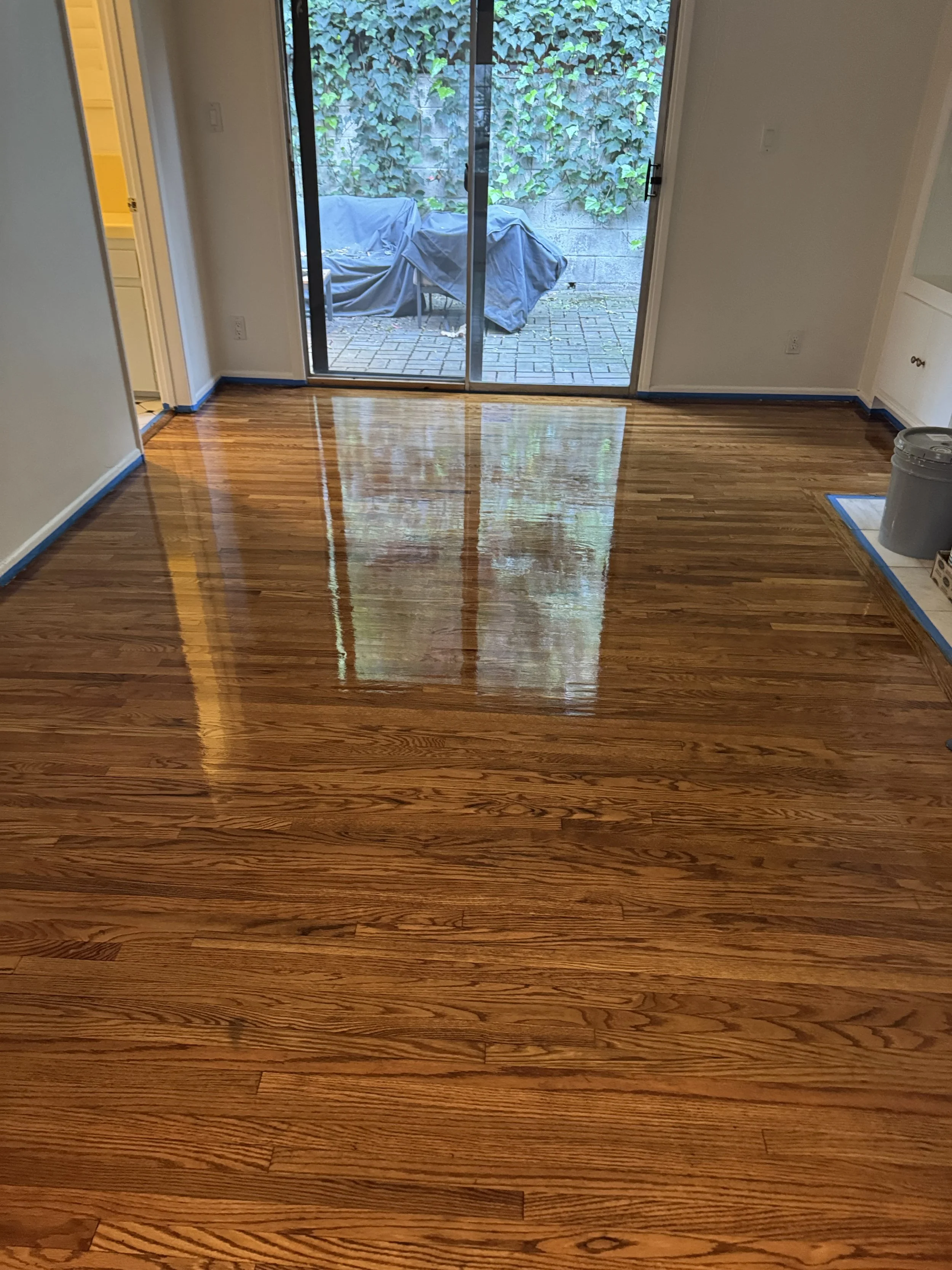 Freshly polished hardwood floor in a living room with sliding glass doors leading to a patio.
