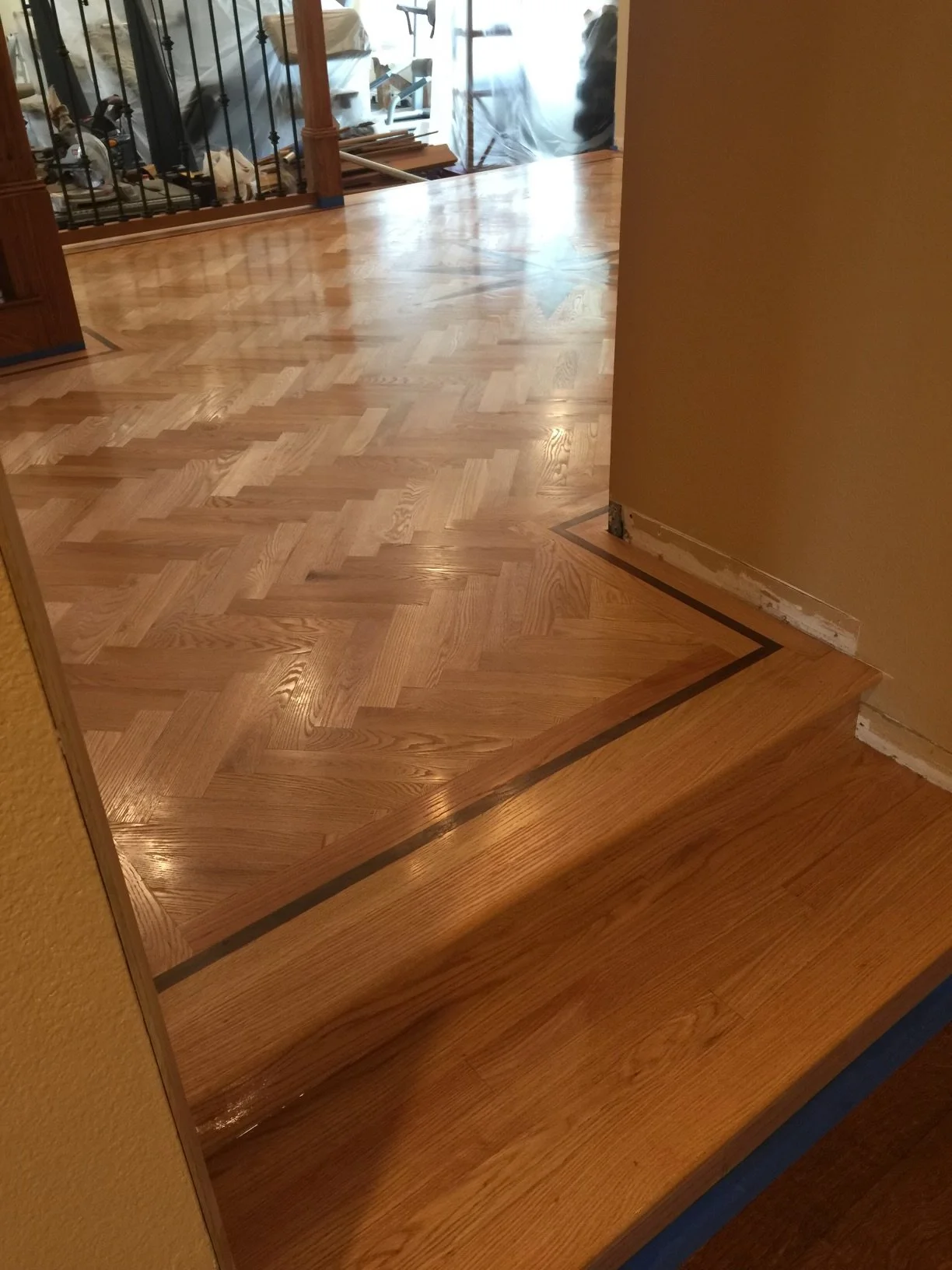 Newly installed hardwood flooring with a step transition between two levels of wood flooring in a home interior, showing a construction or renovation area in the background.