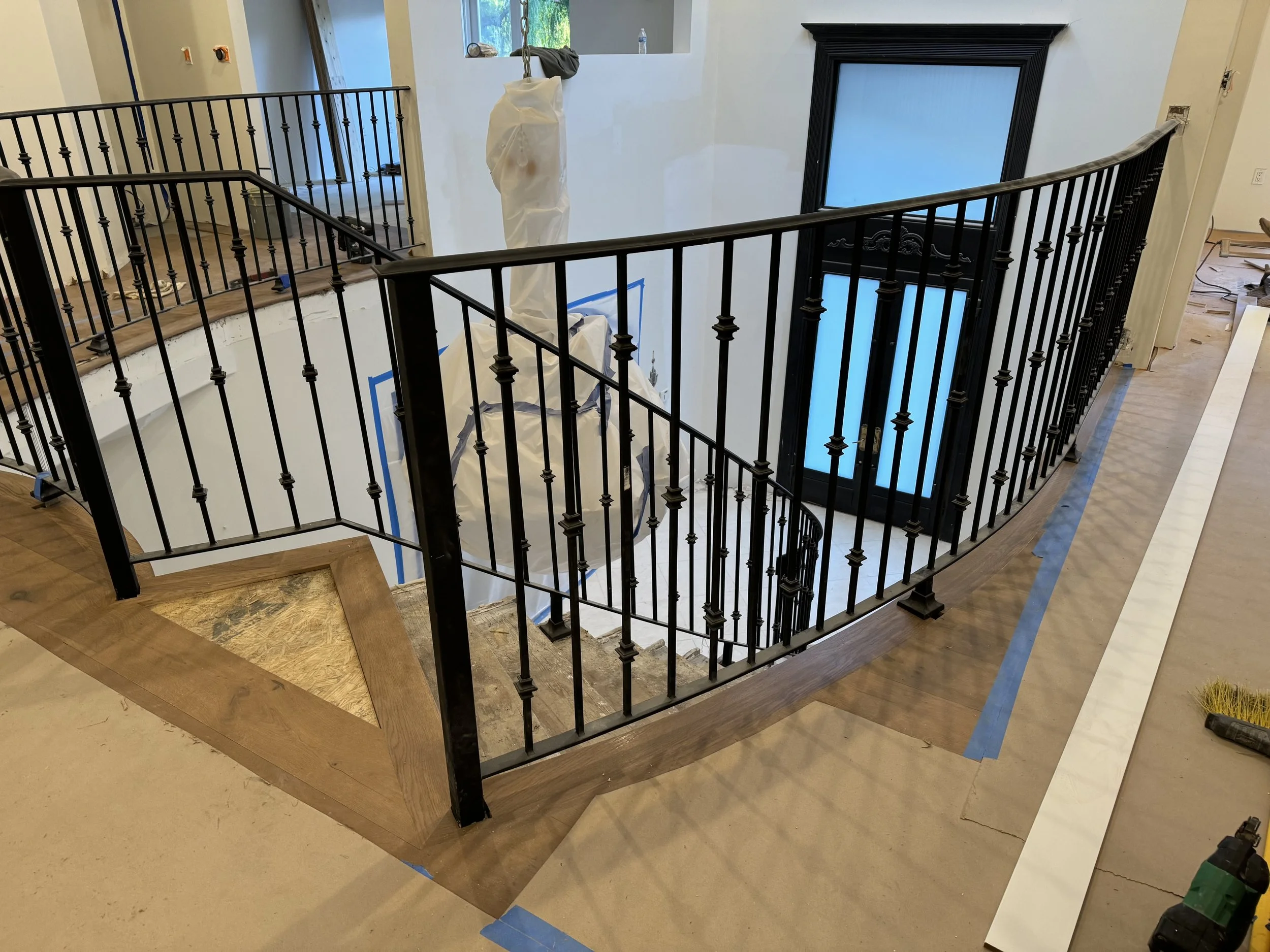 Interior view of staircase with black iron railing, partially finished flooring, and a large window above the staircase in a home renovation setting.