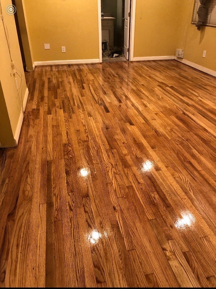 Polished hardwood floor in a living room with yellow walls, a doorway to a laundry area, and a window with blinds.