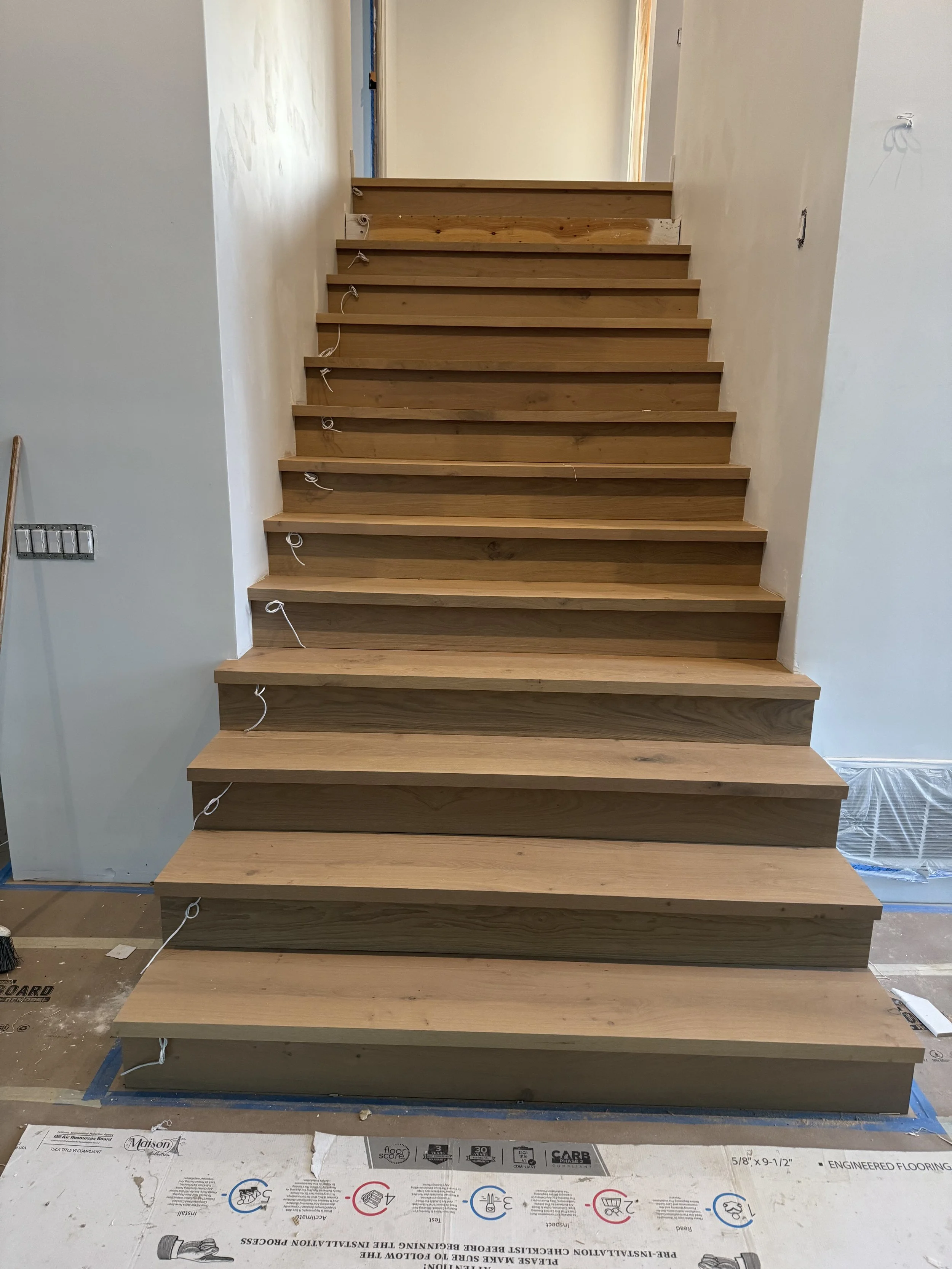 Newly installed wooden staircase with open risers, leading upward to an unfinished area with exposed drywall and trim.