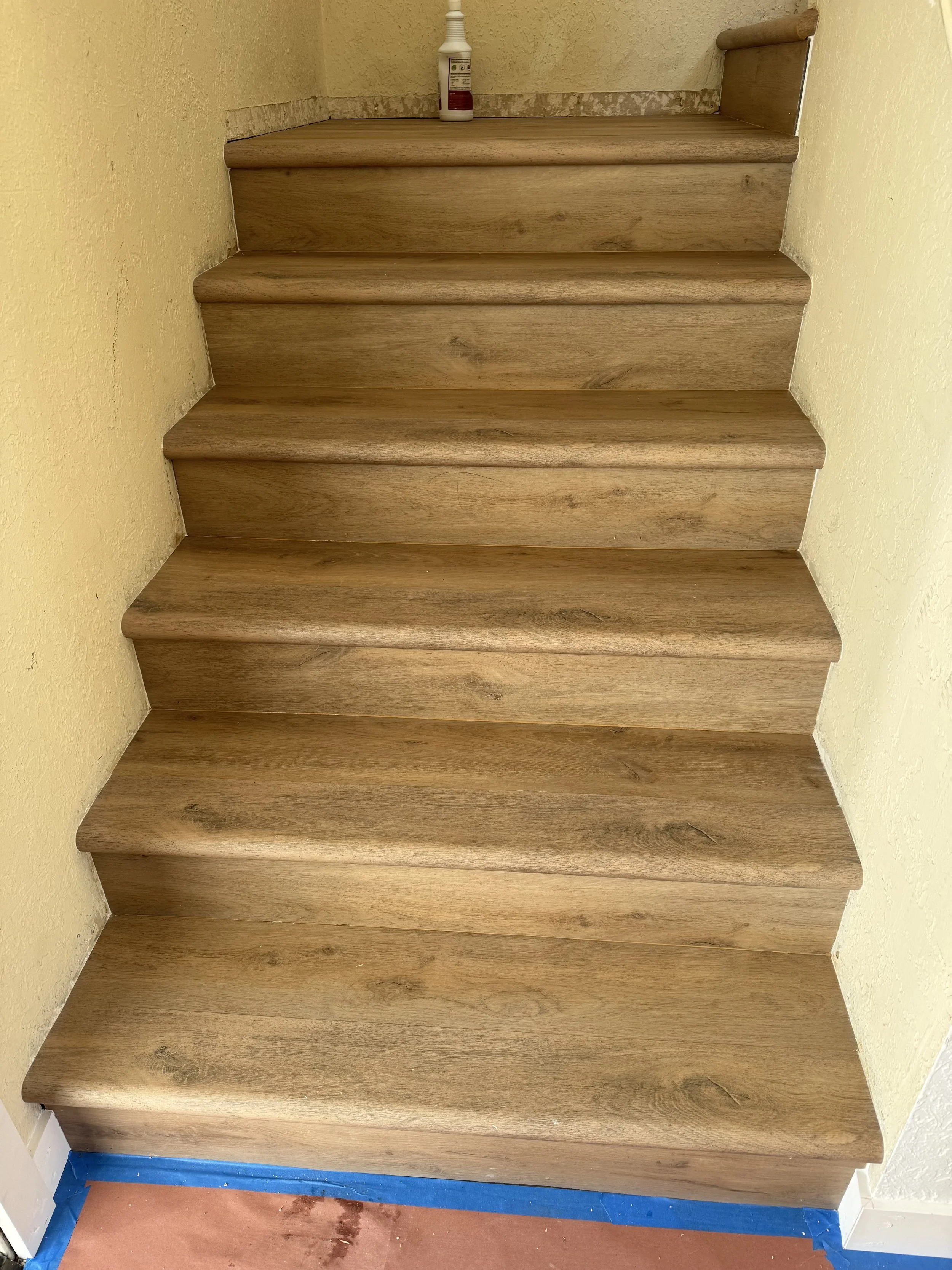 Wooden staircase with yellow walls and a bottle of cleaner on the top step.