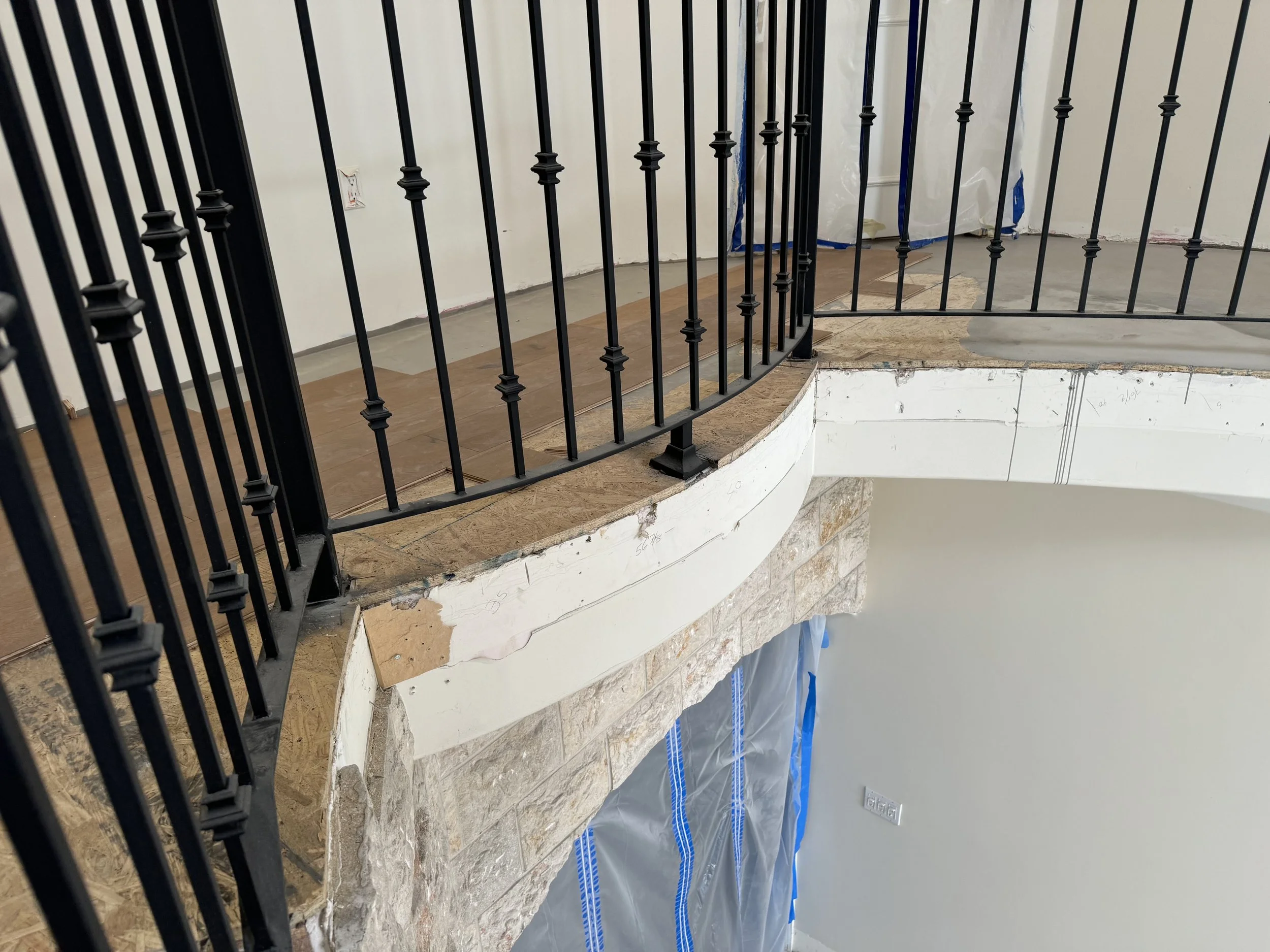 Interior of a building under construction, showing a curved wooden floor and black metal railing, with exposed drywall and construction materials.