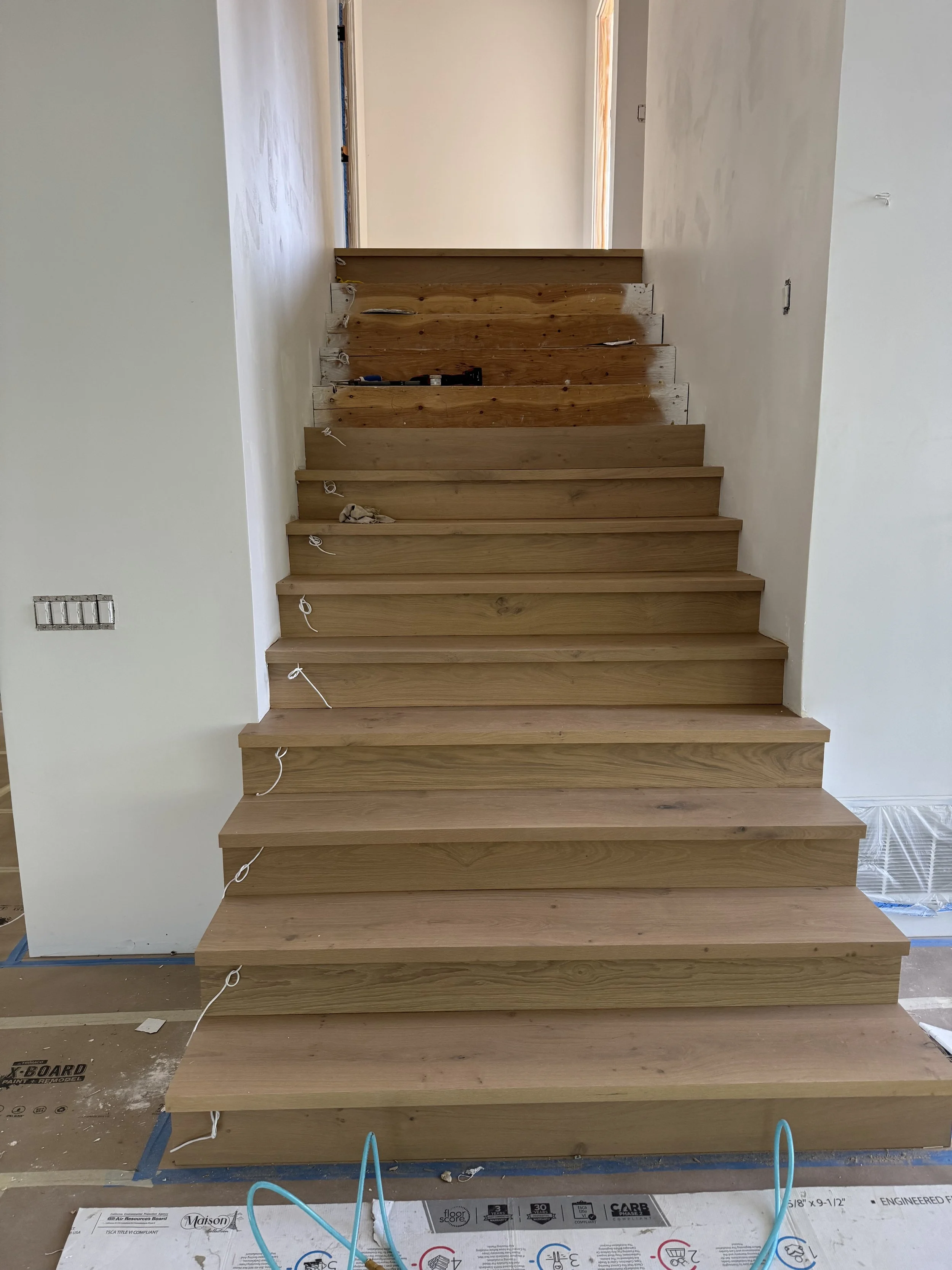 Wooden staircase under construction in a residential interior, with visible wiring and unfinished walls.