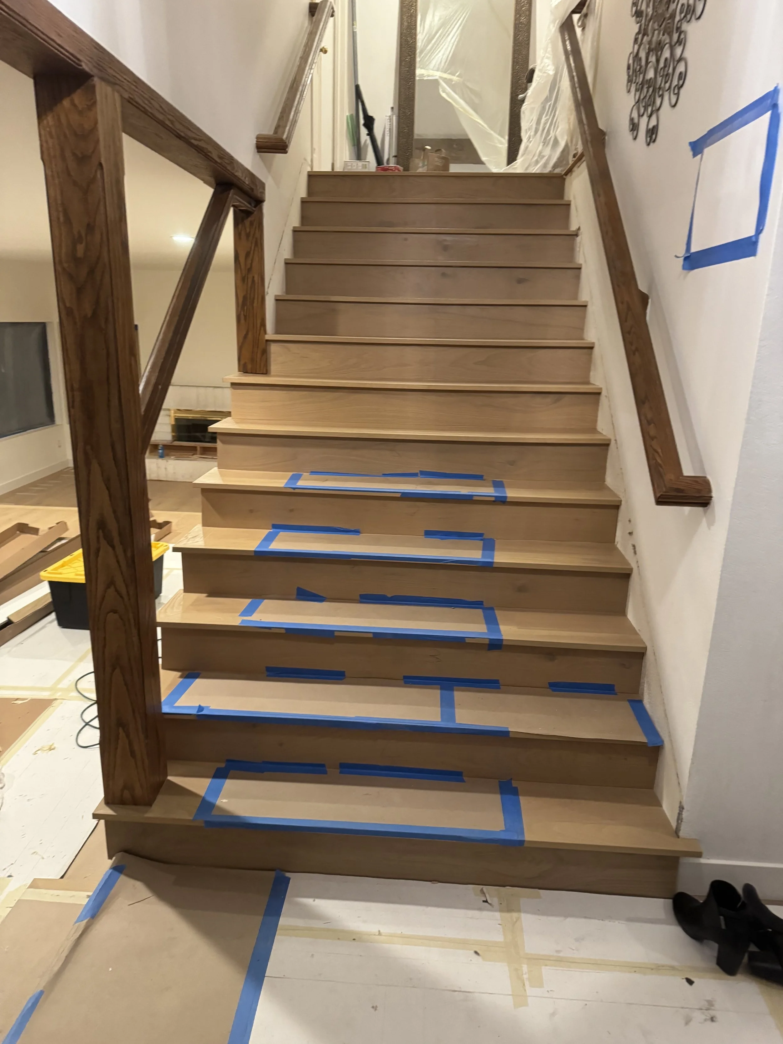 Wooden staircase with blue painter's tape markings on each step, leading to an upper floor, in the process of being constructed or renovated.