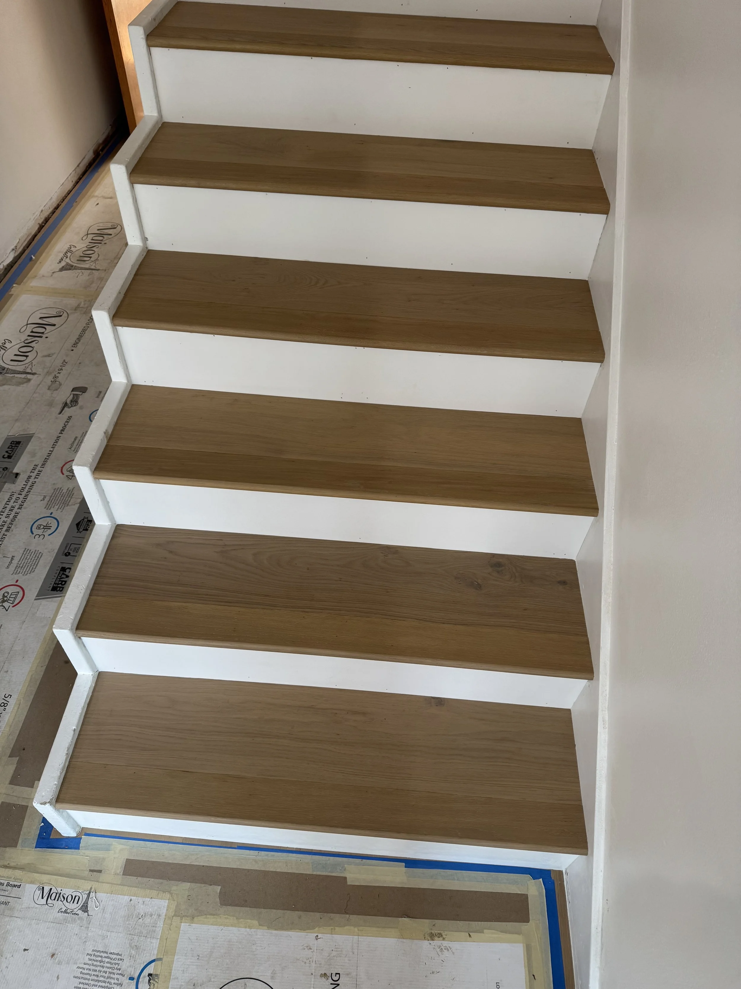 Wooden stairs with white risers in progress, in a room with taped and covered floor.