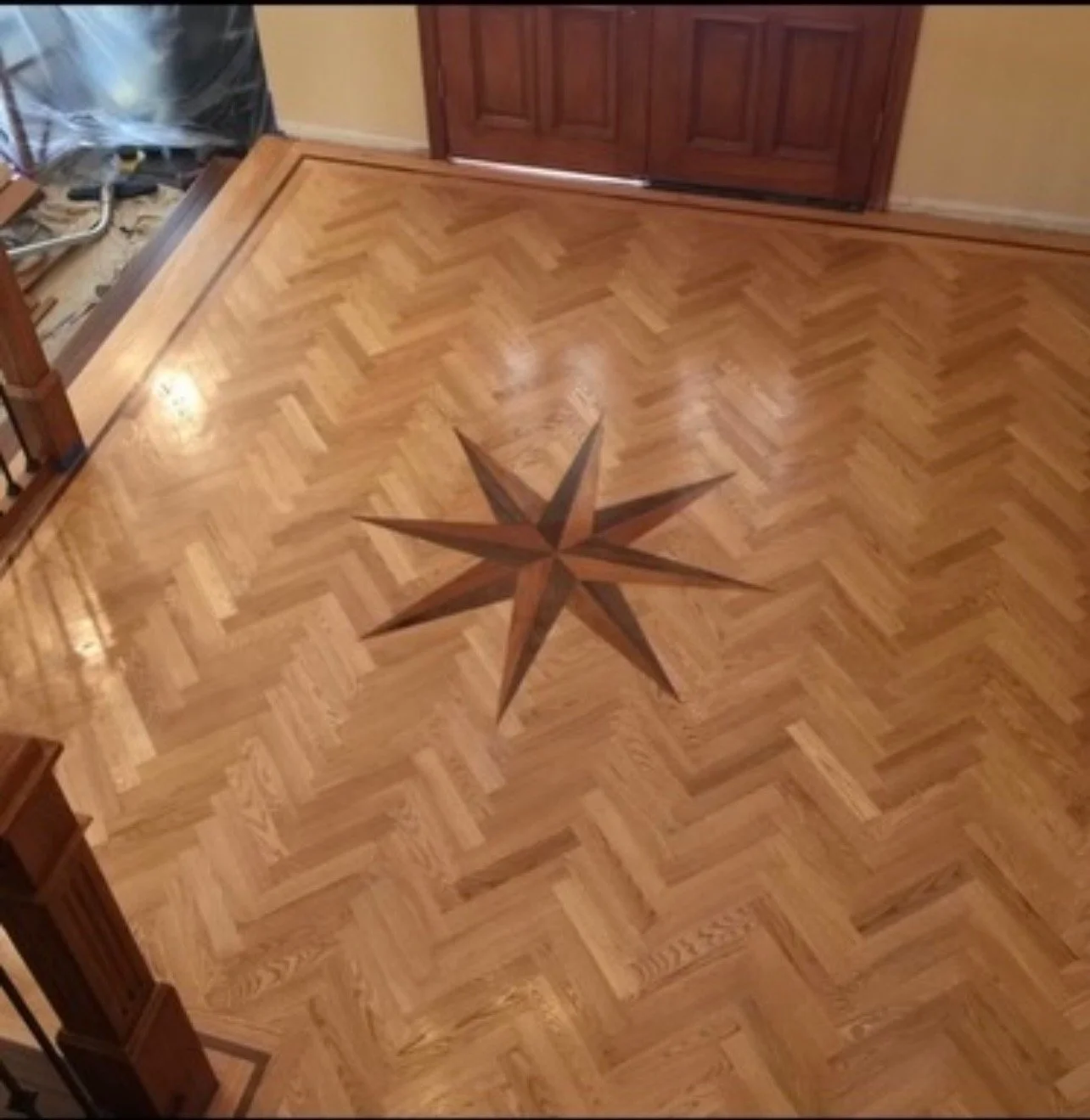 A wooden floor with a decorative star-shaped inlay at the center, surrounded by a herringbone pattern of hardwood planks.