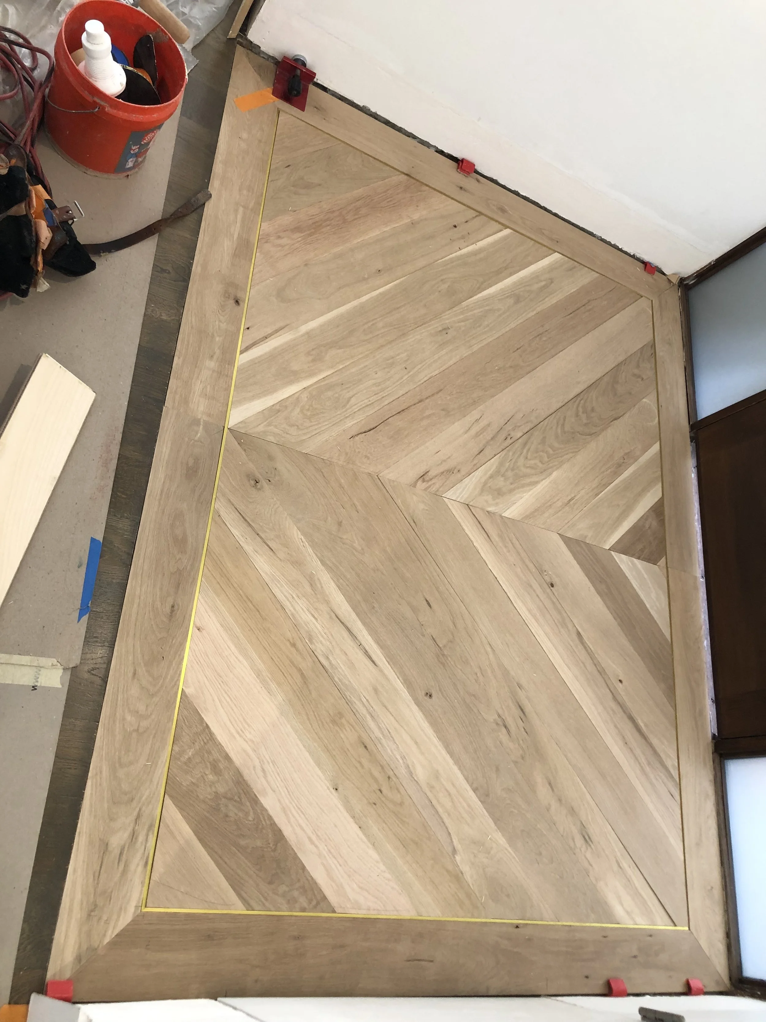 Wooden flooring being installed in a corner, with alignment tools and construction materials nearby.