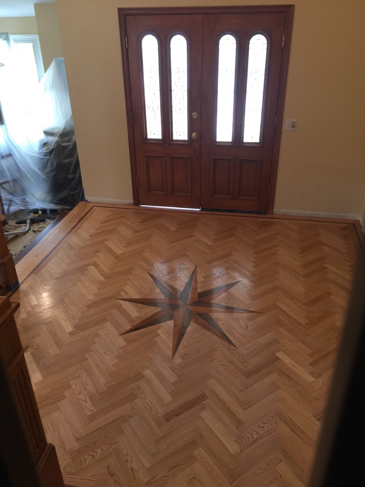 View of a hardwood floor with a star-shaped inlay design in the center, near a wooden front door with glass panels.