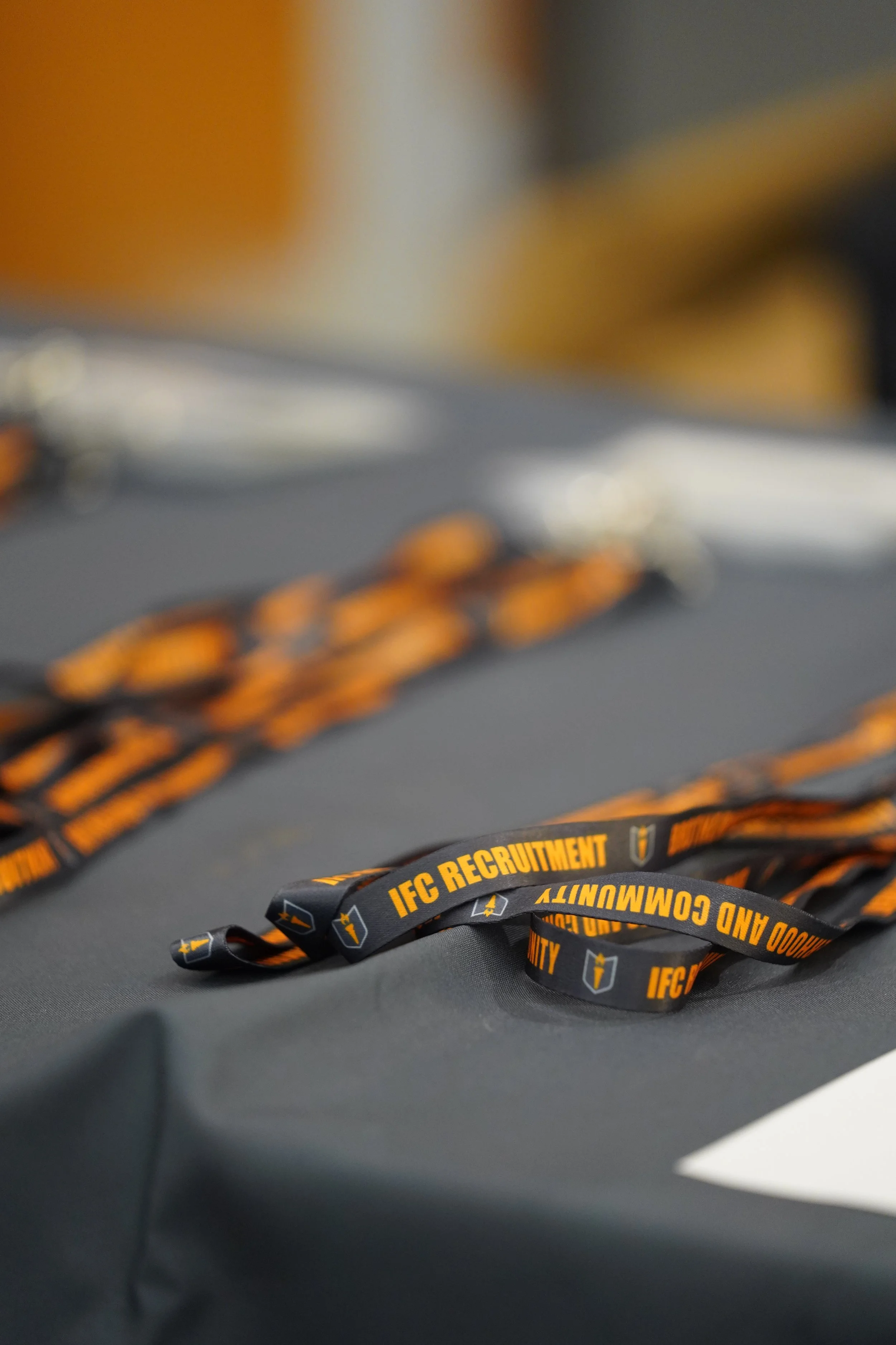 Black lanyard with yellow text reading 'IFC RECRUITMENT' and small shield logos, placed on a dark gray surface.