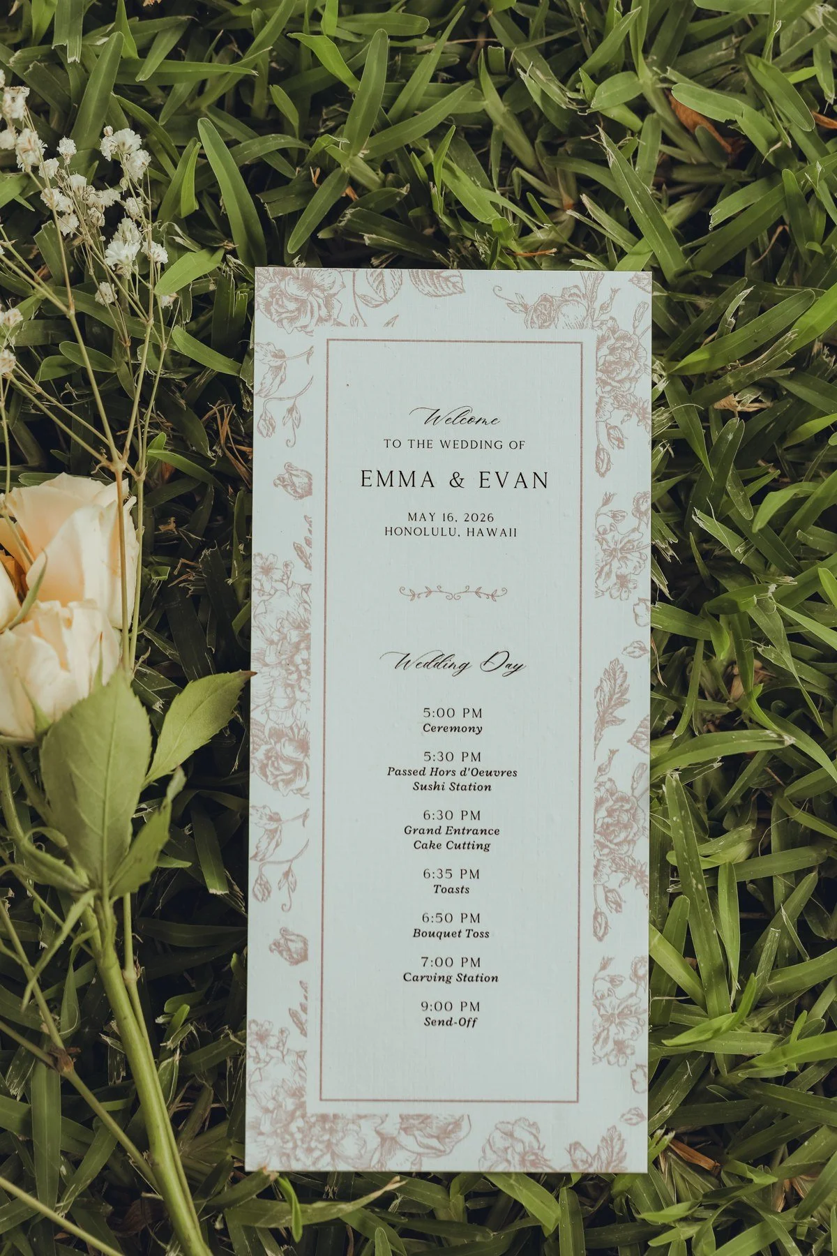 Emma and Evan’s floral-bordered wedding schedule card displayed among garden greenery.