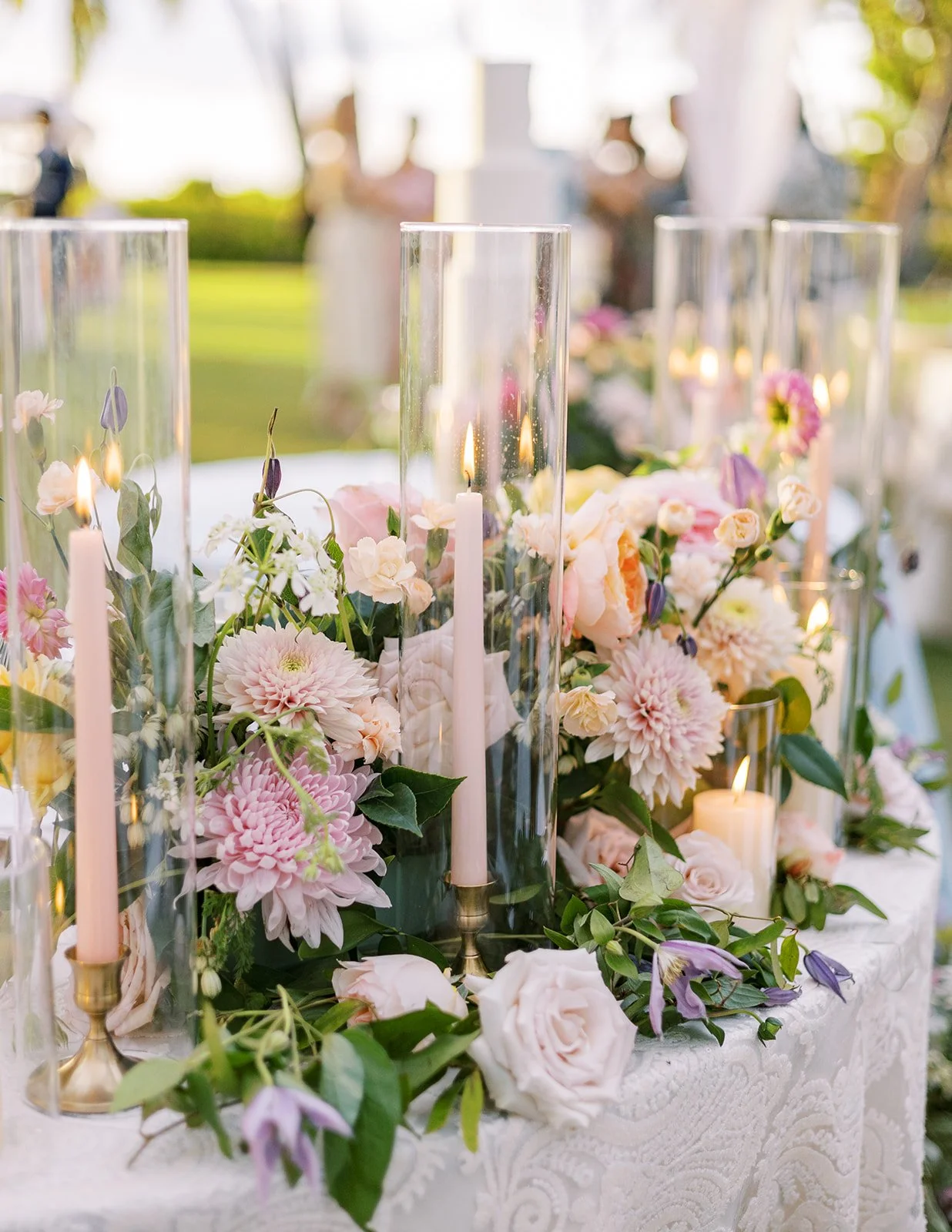 Wedding table centerpiece with pink and white flowers, greenery, and tall glass candle holders.
