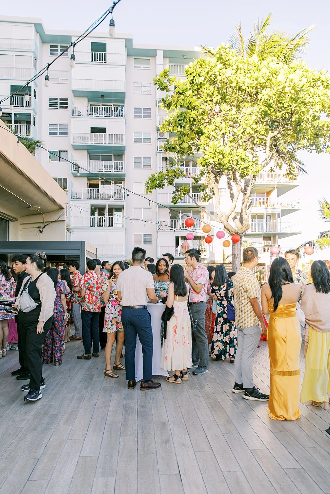 Guests mingling at an outdoor social event with colorful attire, string lights, and tropical decor.