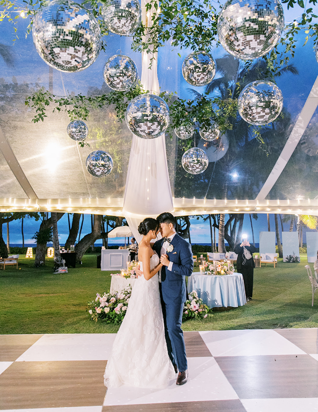 Bride and groom dancing under hanging disco balls and draped tent decor during an outdoor evening reception.