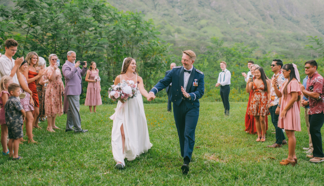 Bride and groom walking hand in hand through applauding guests during an outdoor celebration.