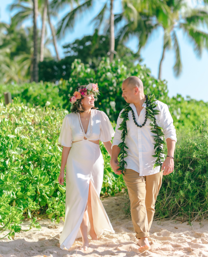 Couple walking hand in hand on a sunny beach surrounded by tropical greenery.
