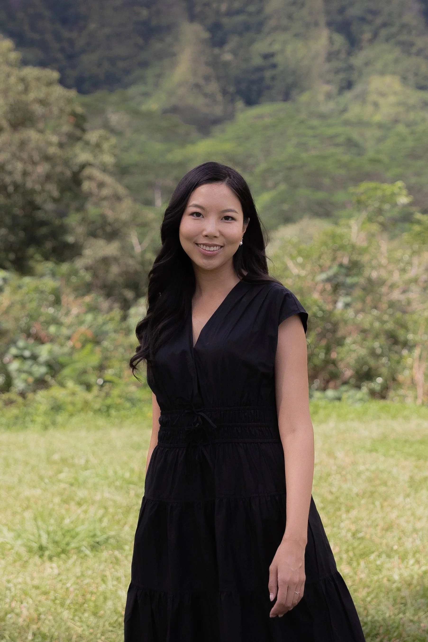 Portrait of Priscilla Bella, founder and lead planner, standing outdoors in a black dress with greenery in the background.