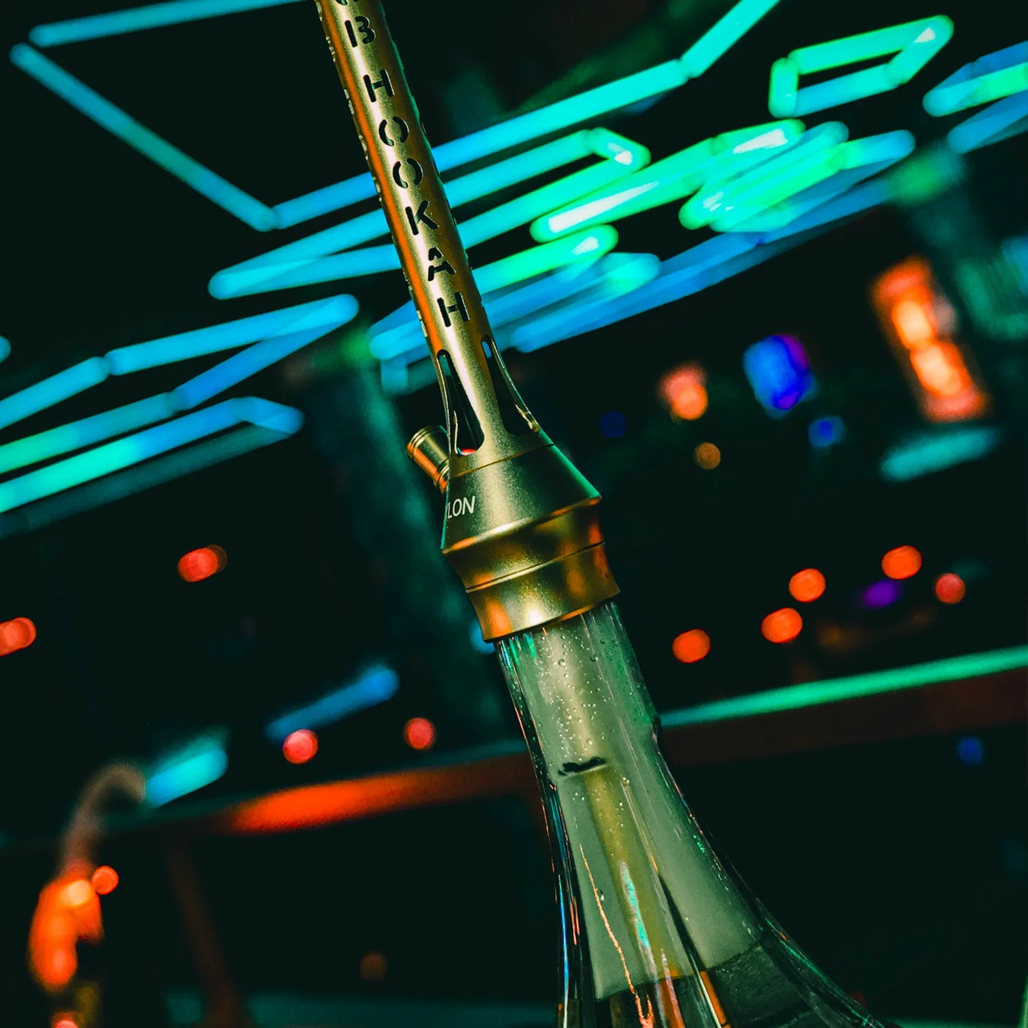 Close-up of a hookah with a glass base, set against a background of neon lights in various colors.