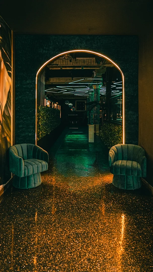 A stylish hallway with neon lighting, green velvet chairs, and a glittery gold floor.