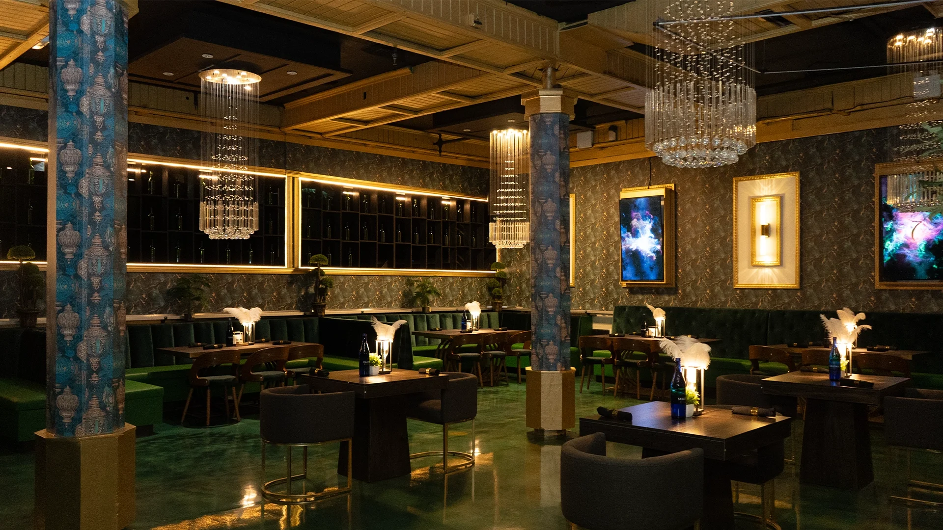 Interior of an upscale restaurant or lounge with dark green seating, modern art on the walls, chandeliers, and dim lighting.