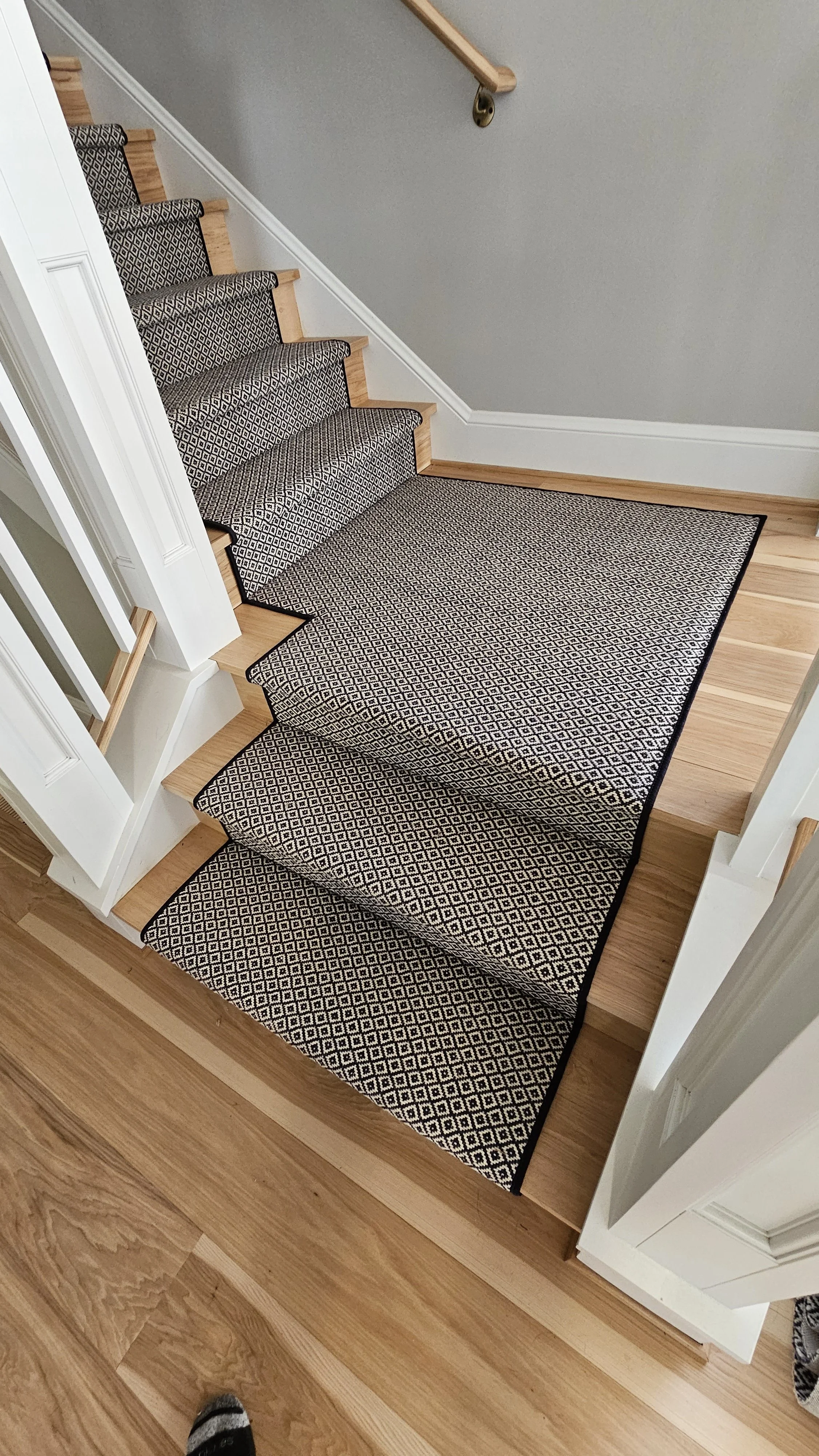 A staircase with wooden steps and a black and white diamond patterned runner rug in a home interior.
