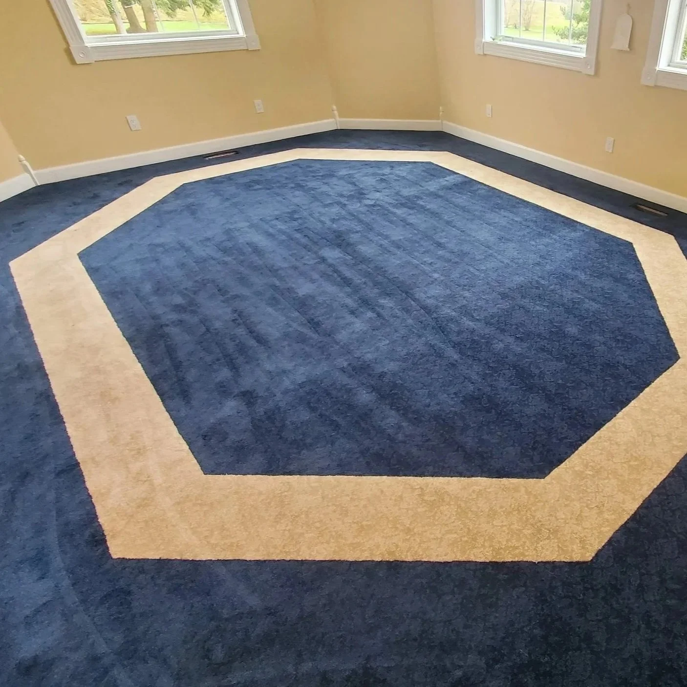 Empty room with yellow walls, three windows, and a blue and beige hexagonal carpet.