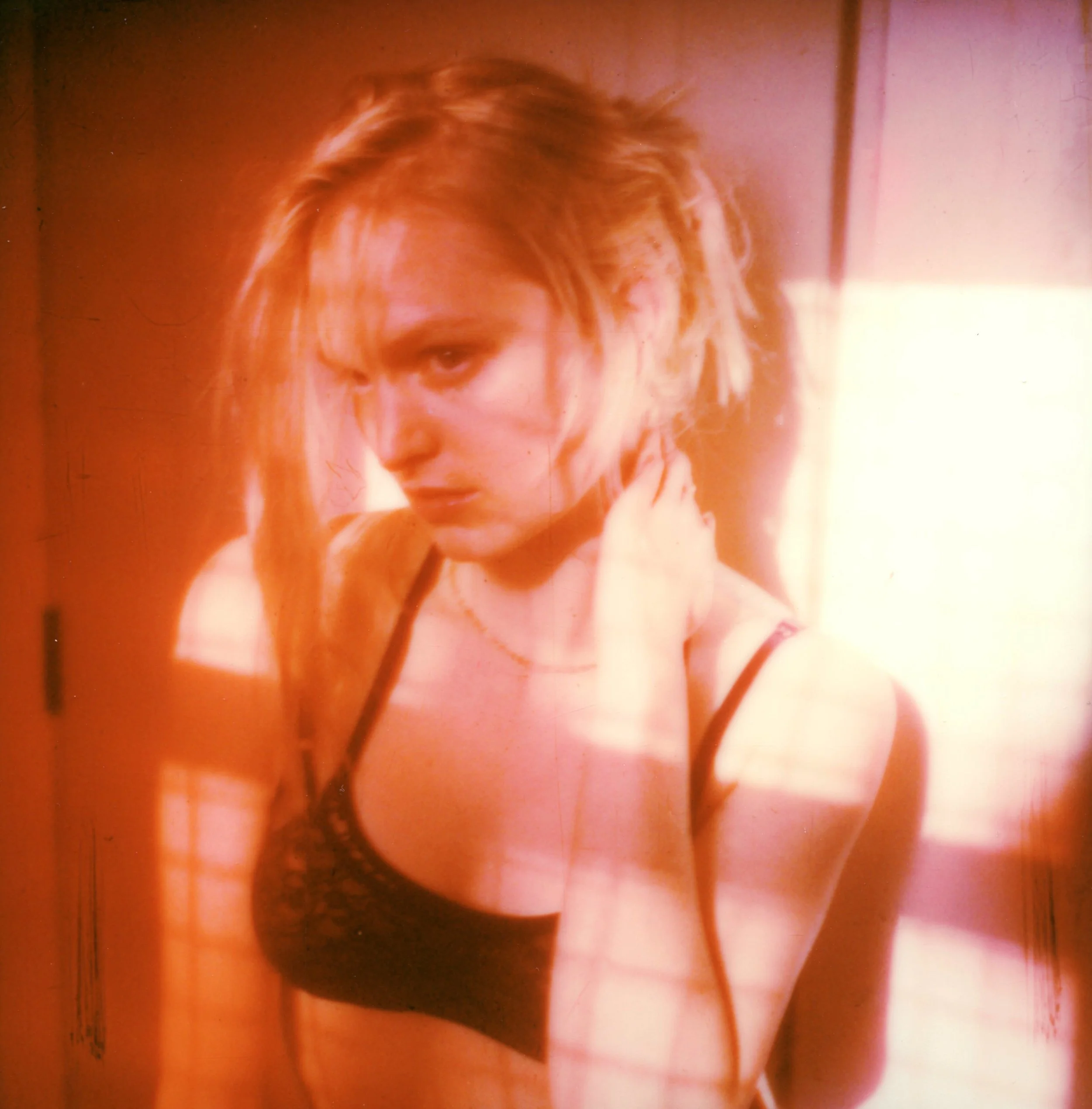 Mujer joven con cabello rubio y largo, con ropa de lencería negra, en un ambiente con luz cálida y sombras proyectadas.