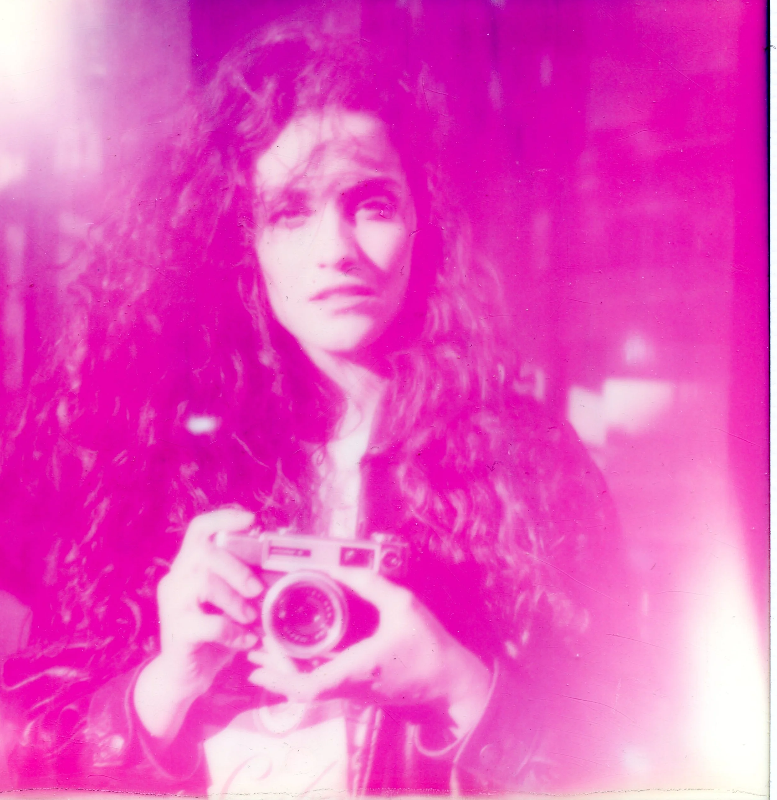 Una mujer con cabello rizado sostiene una cámara fotográfica, observando hacia la izquierda.